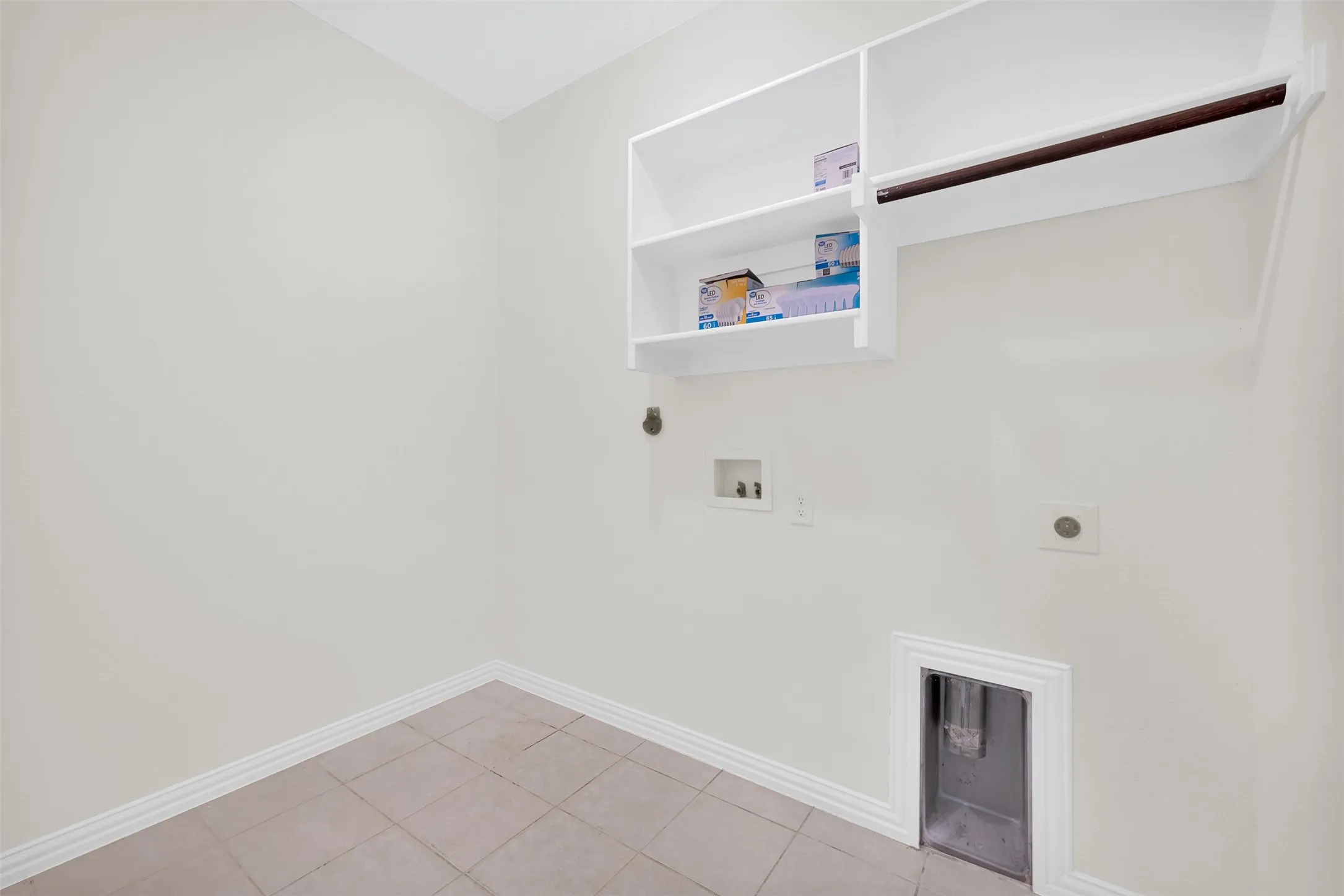 Laundry area featuring neutral wall paint, tile flooring, white baseboards, and built-in white shelving with a hanging rod