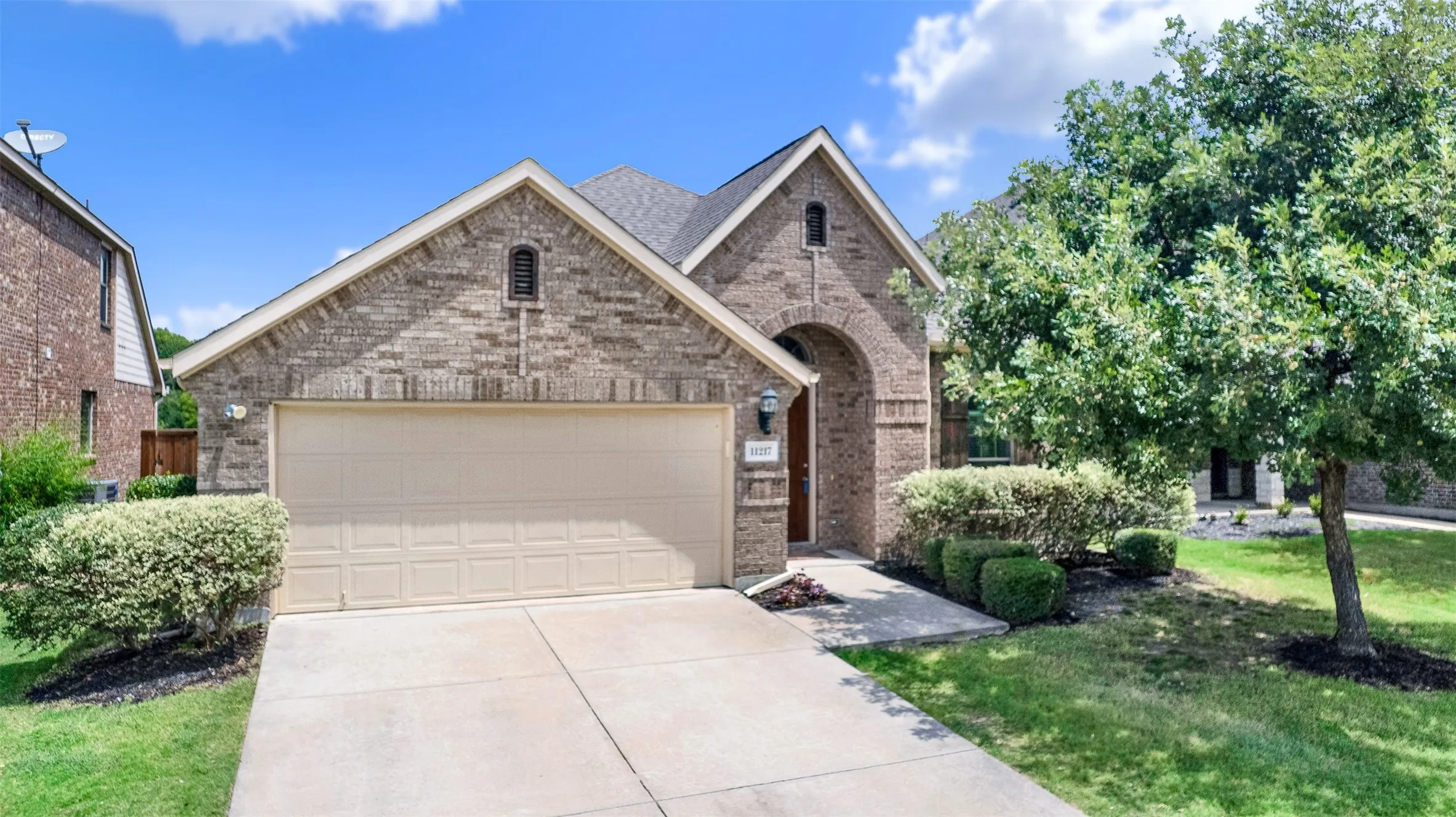 Brick exterior with an arched entryway, gabled rooflines, an attached garage, and a concrete driveway