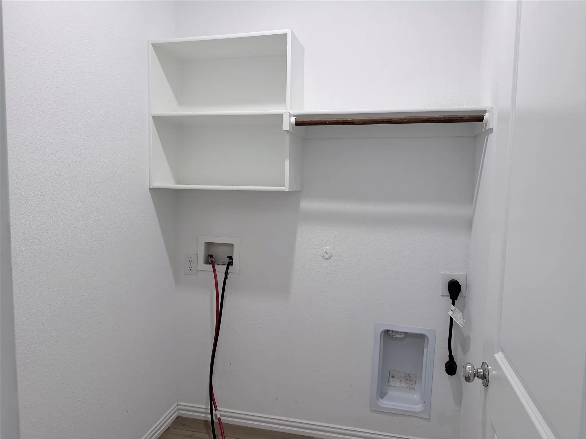 Dedicated laundry area featuring white walls, built-in shelving, a clothes hanging rod, electrical outlets, and wood-finish flooring