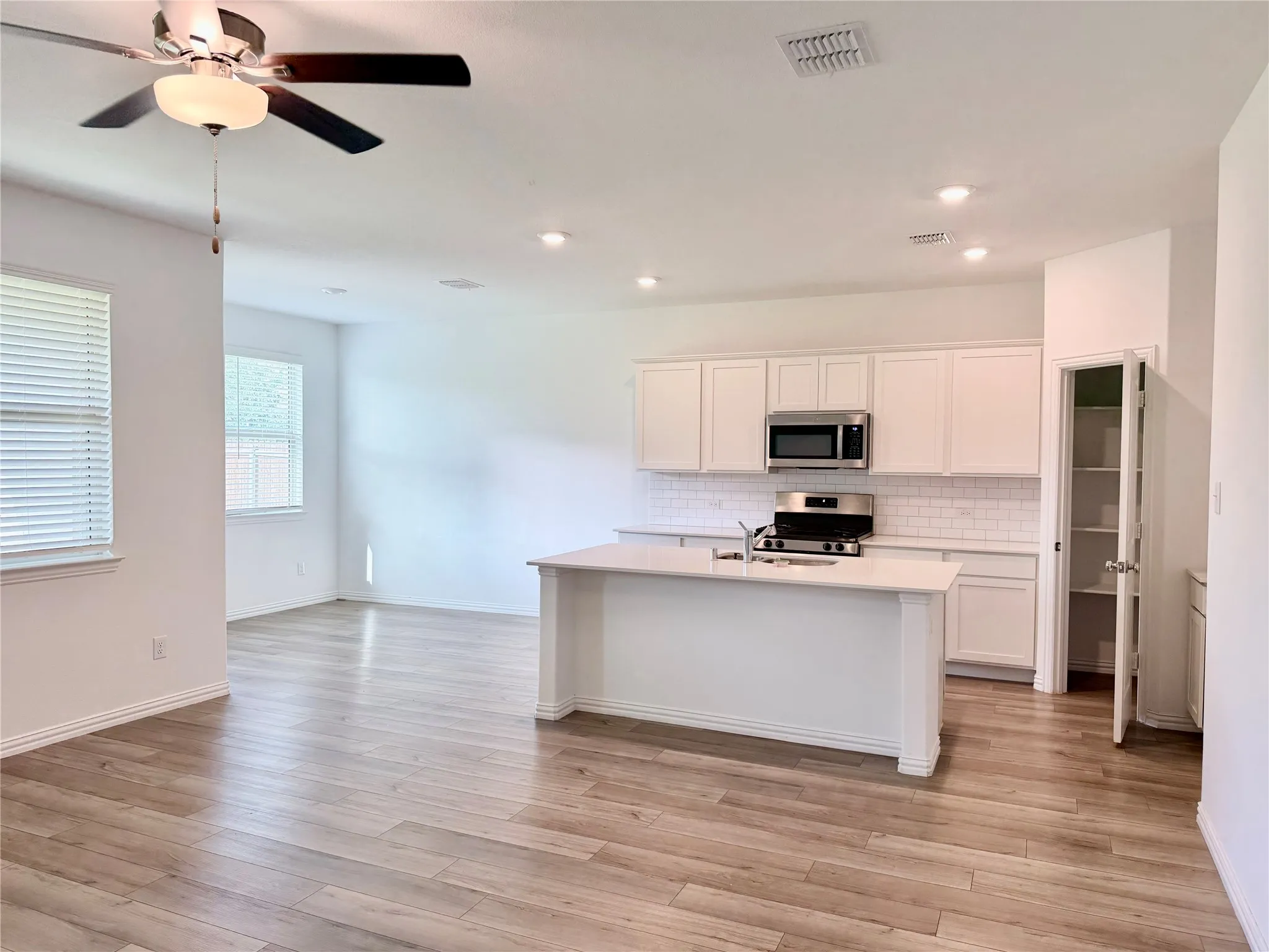 Open-concept kitchen and living area featuring wood-finish flooring, recessed lighting, a white subway tile backsplash, stainless steel appliances, and a kitchen island with sink