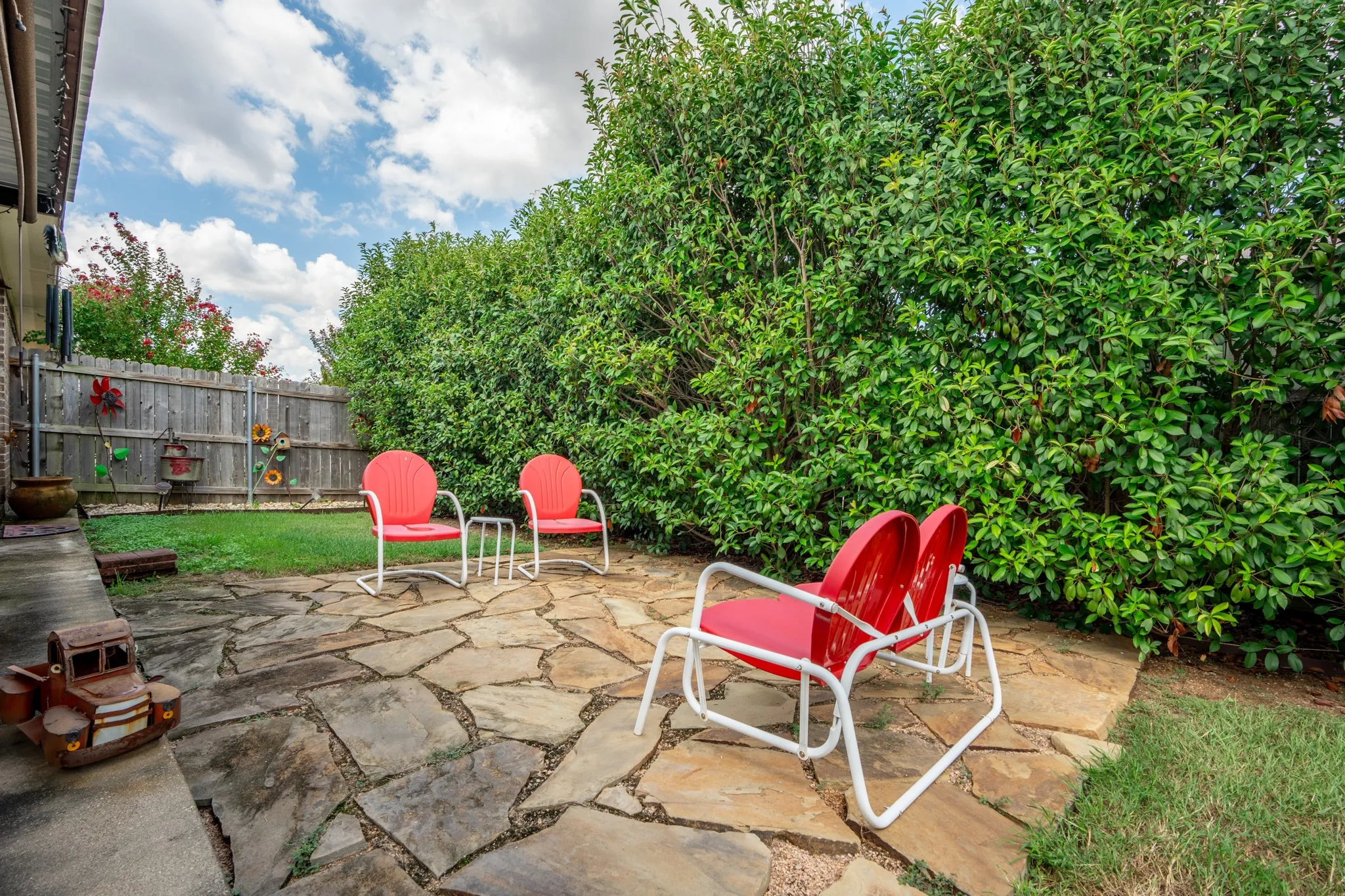 Flagstone patio featuring an expansive hedge, a manicured lawn, and a wood-panel fence