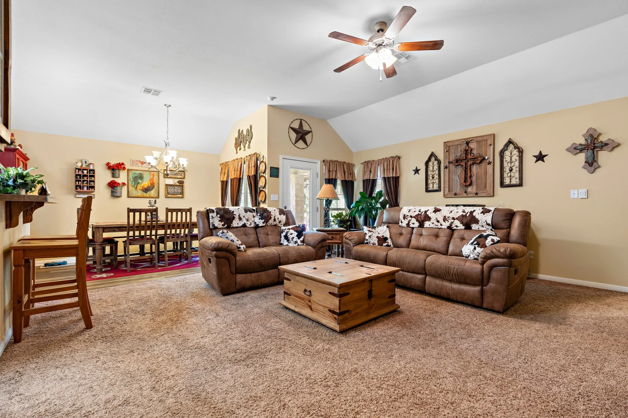 Vaulted ceiling featuring a ceiling fan with light fixture, carpeted flooring, and a dining area with wood-finish flooring