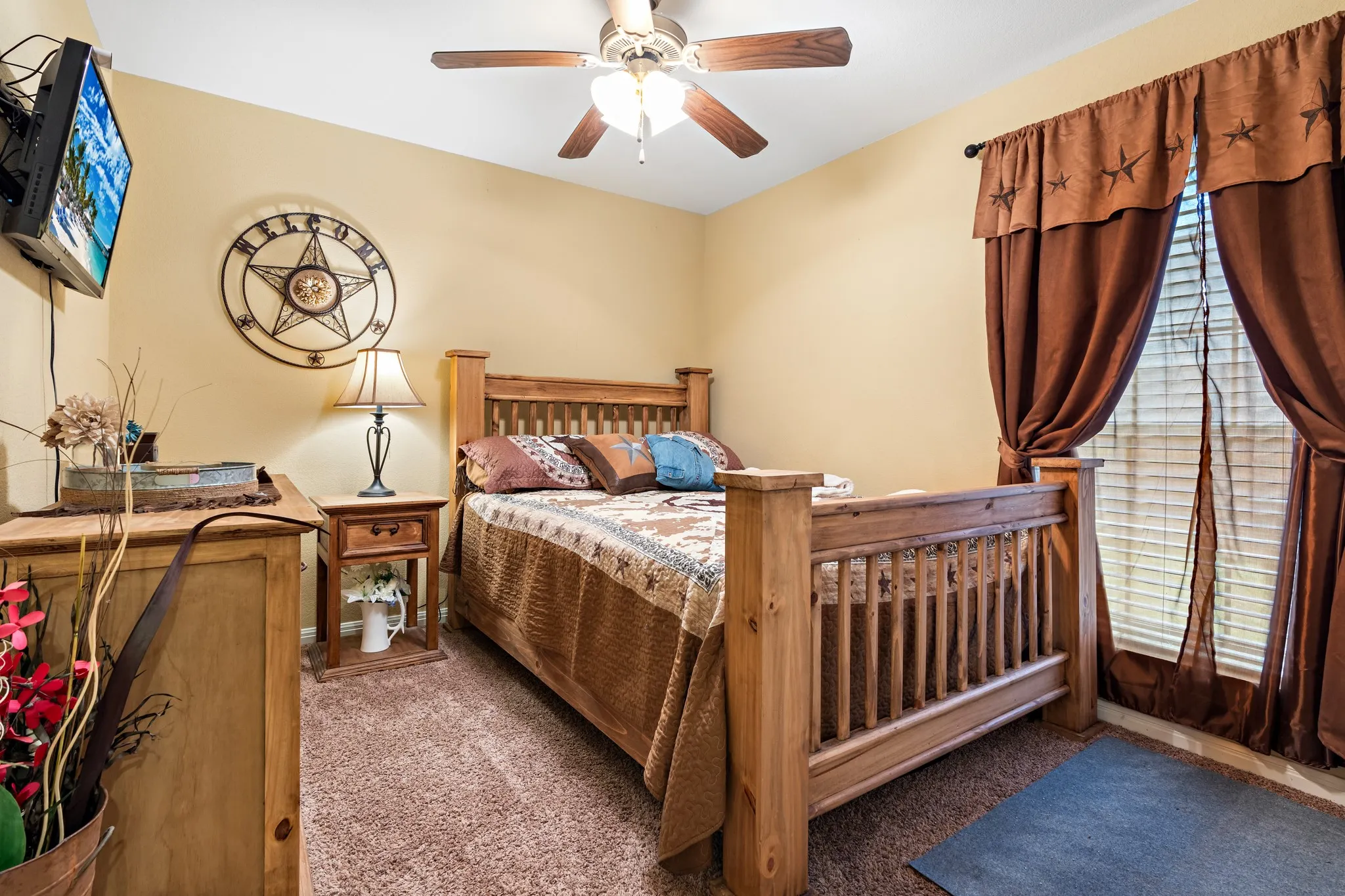 Carpeted room featuring a ceiling fan, window with blinds and drapes, and a wall-mounted television bracket