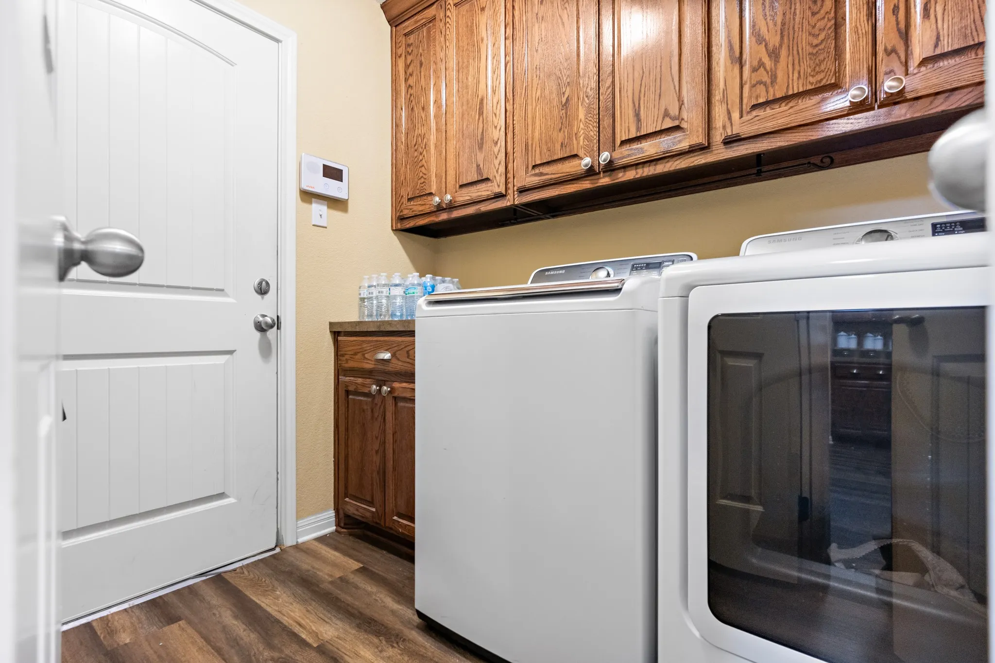 Dedicated laundry space featuring wood-finish flooring, white paneled door, and built-in upper and lower cabinetry with a countertop