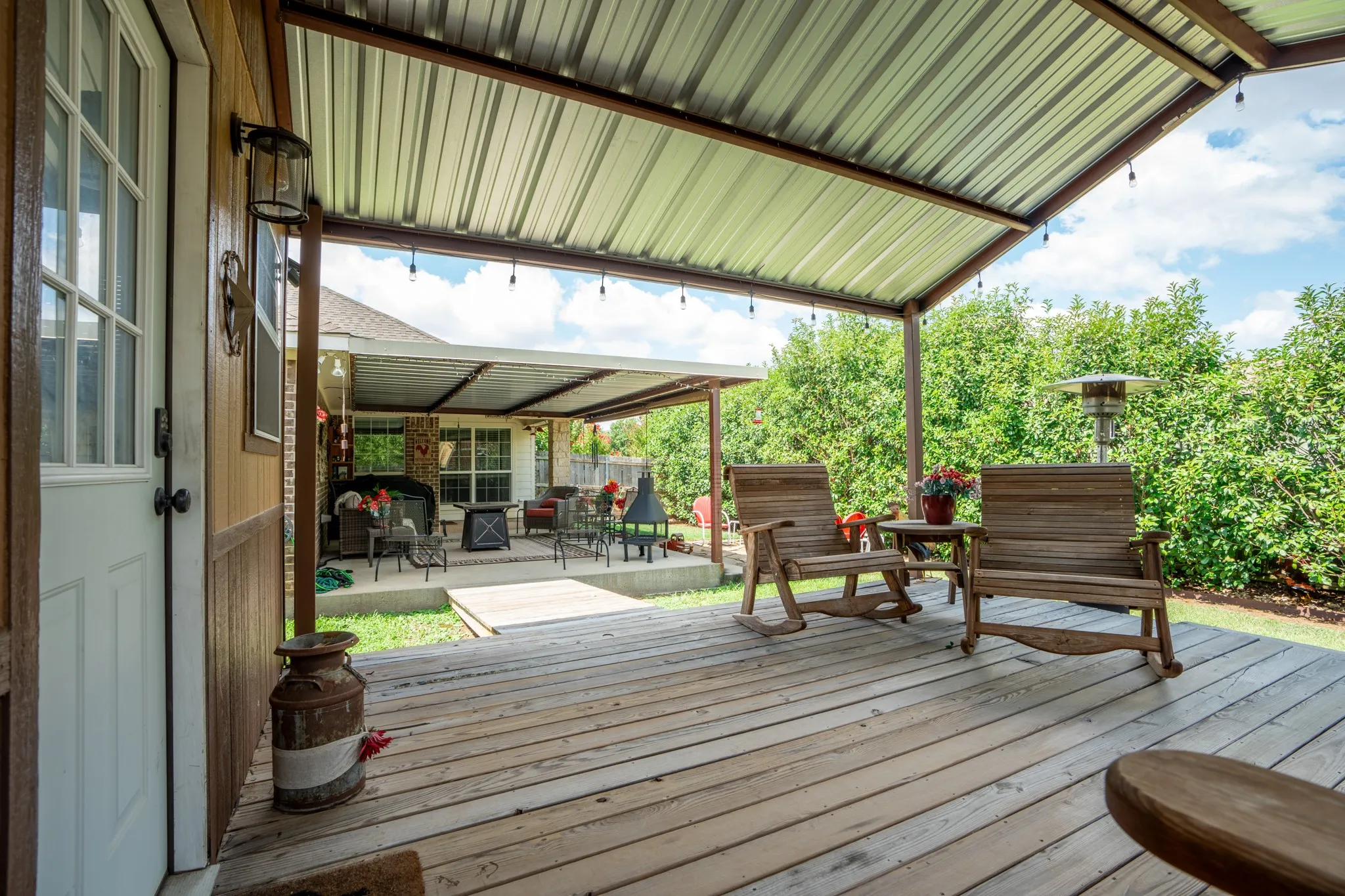 Expansive outdoor covered patio featuring wood-finish decking, a corrugated metal roof, and string lighting