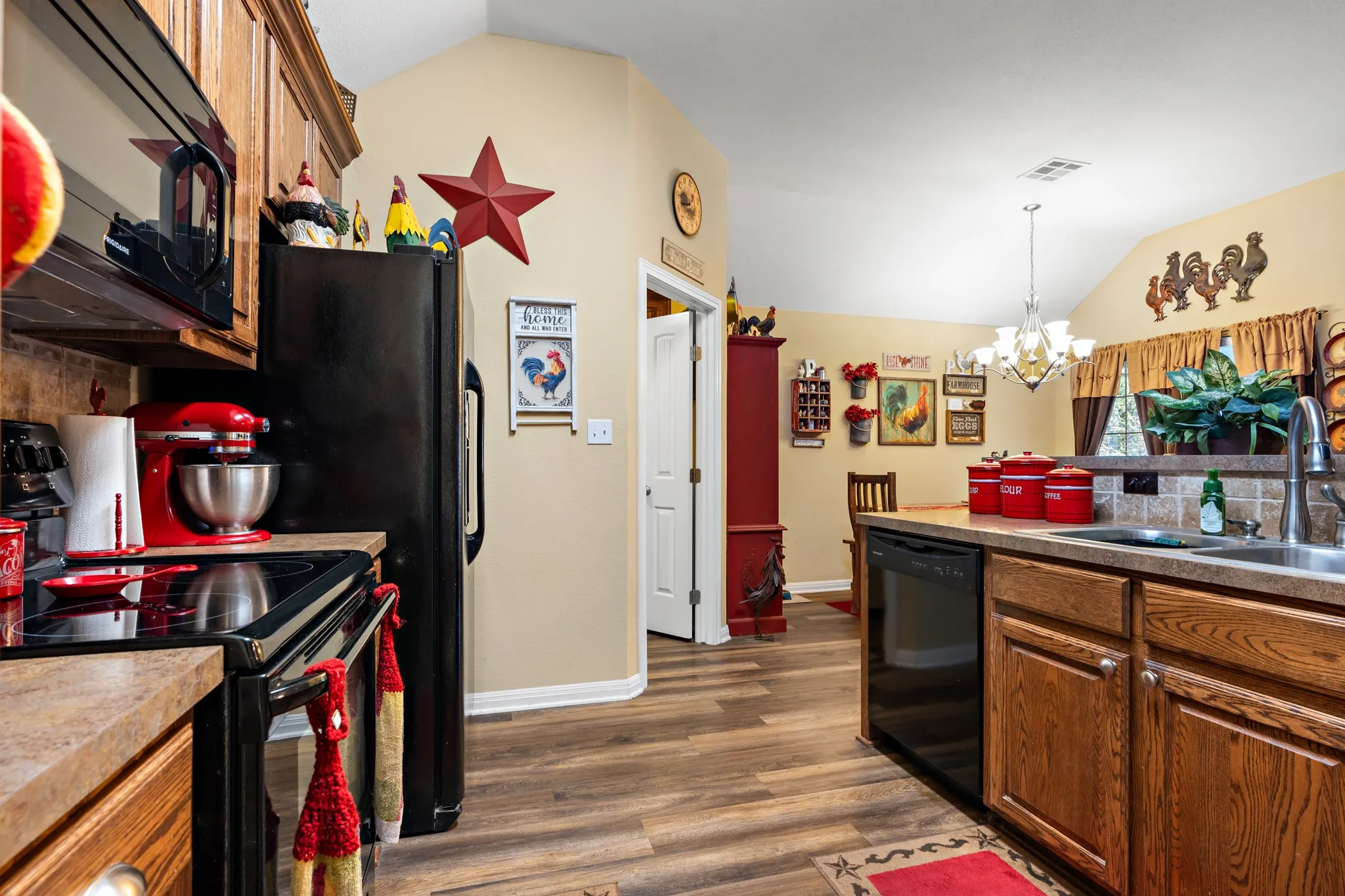 Kitchen featuring wood-finish flooring, oak cabinetry, black appliances, and a pass-through counter with a double-basin sink