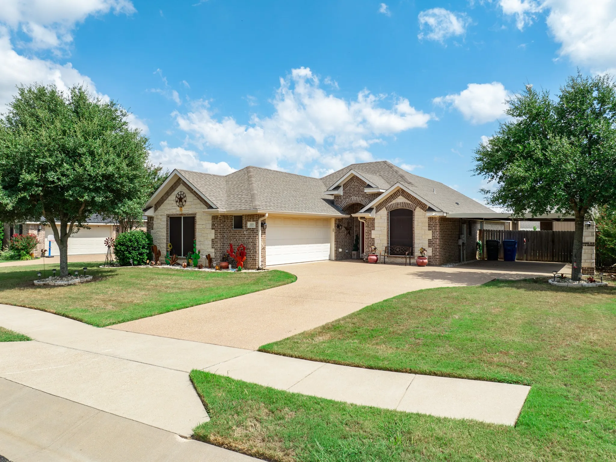 Exterior featuring light-toned brick and stone veneer, a covered entrance, two-car garage, and an attached carport