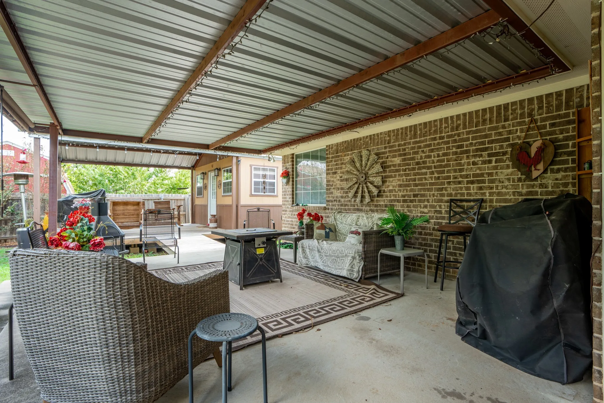 Expansive covered patio featuring a corrugated metal roof, concrete flooring, and a brick exterior wall
