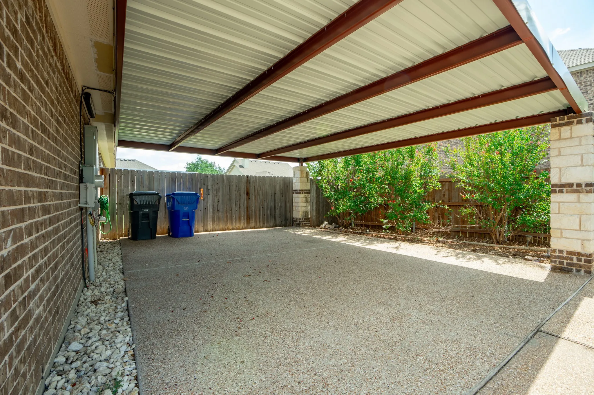 Covered patio featuring a corrugated metal roof with exposed structural beams, a brick exterior wall, and an exposed aggregate concrete slab