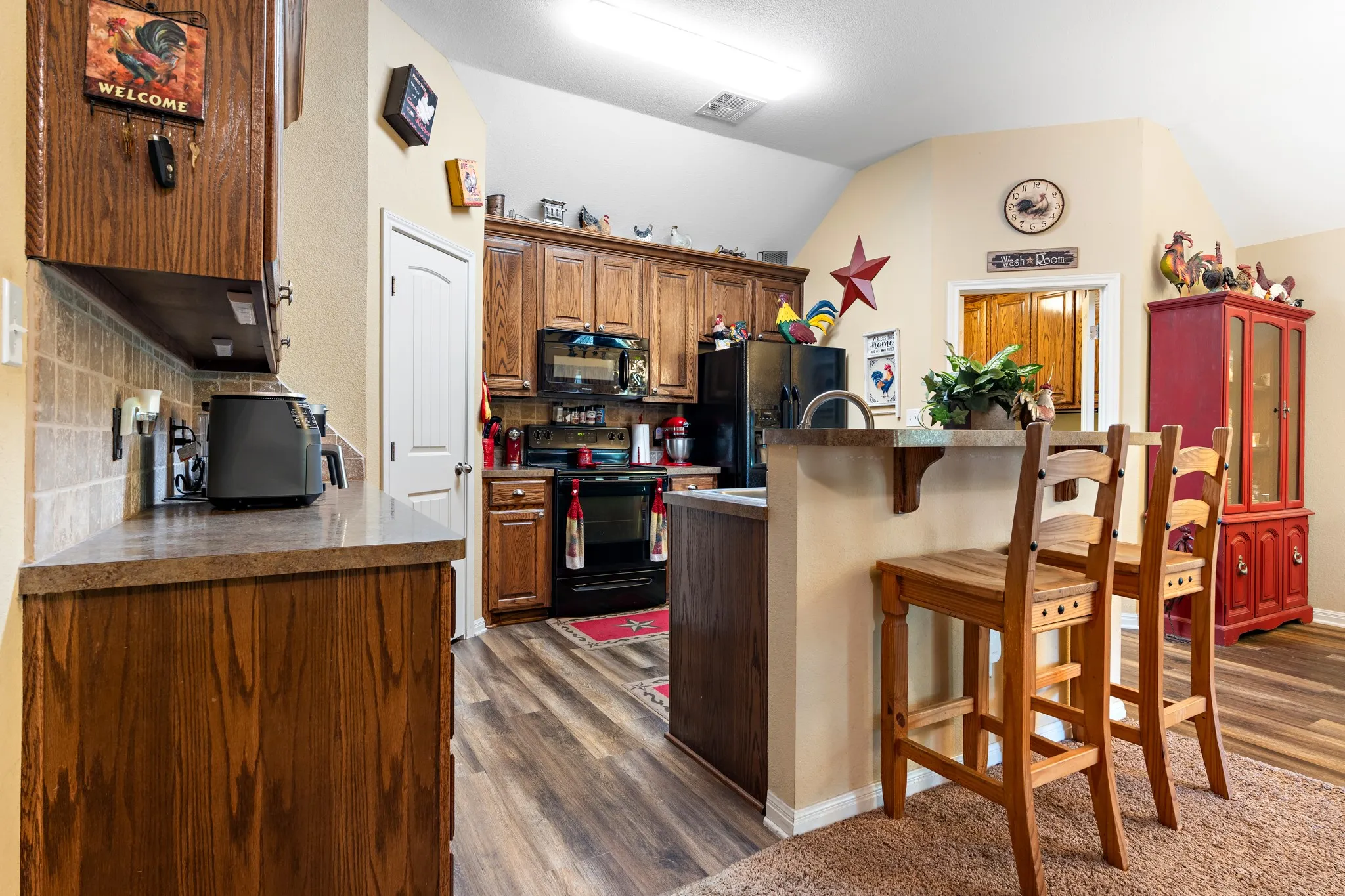 Kitchen featuring wood-finish flooring, wood cabinetry, a tiled backsplash, and black appliances