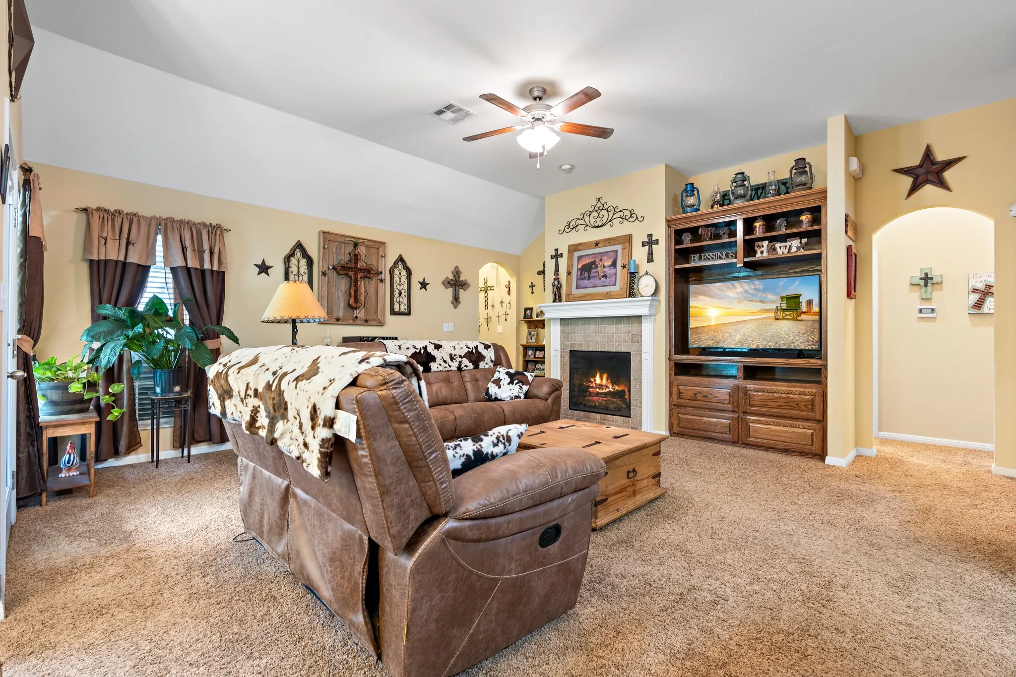Open-concept living space featuring a built-in media center with shelving, a fireplace with a stone surround, an arched entryway, and a ceiling fan