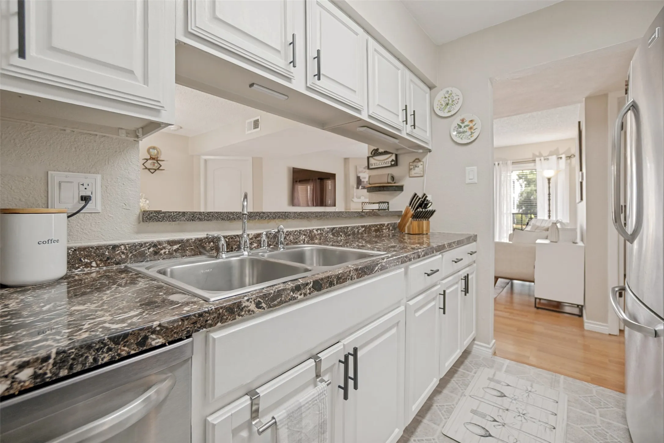 Kitchen featuring white cabinetry, dark stone-look countertops, stainless steel double basin sink, and a pass-through window to an adjacent room