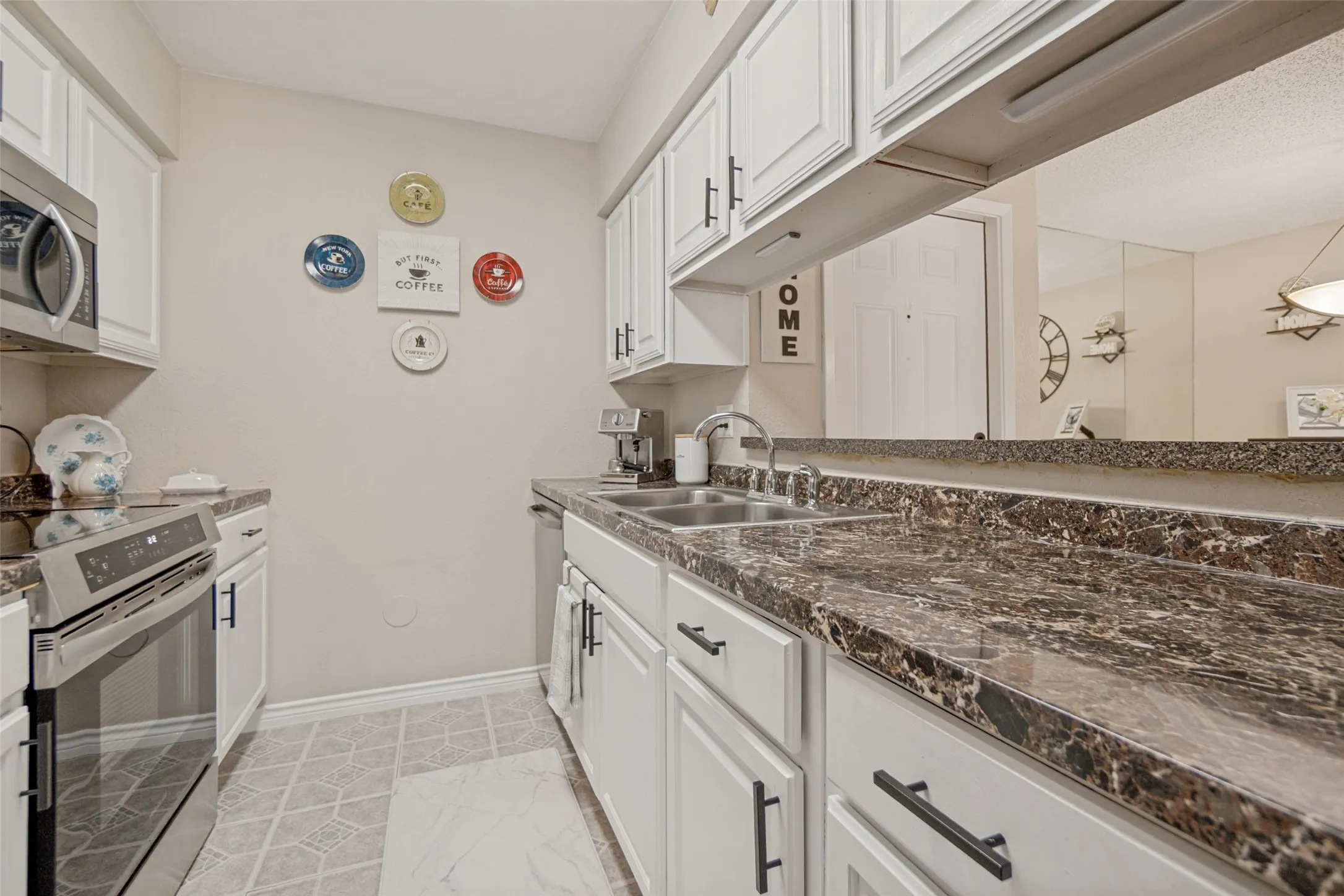 Kitchen featuring white cabinetry with dark hardware, stainless steel appliances, a double basin sink, and patterned countertops