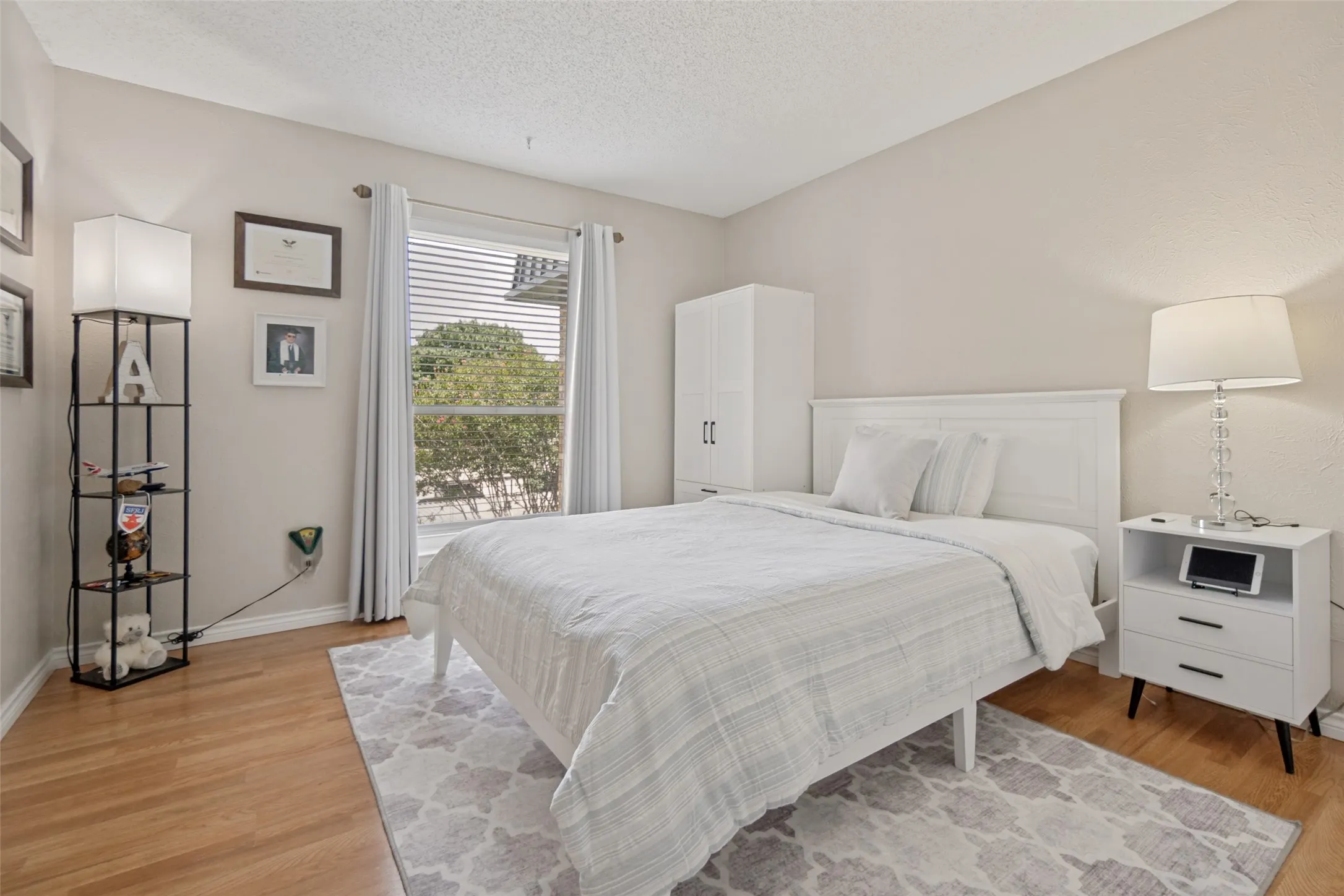 Room featuring wood-finish flooring, a window with horizontal blinds, and neutral-toned walls