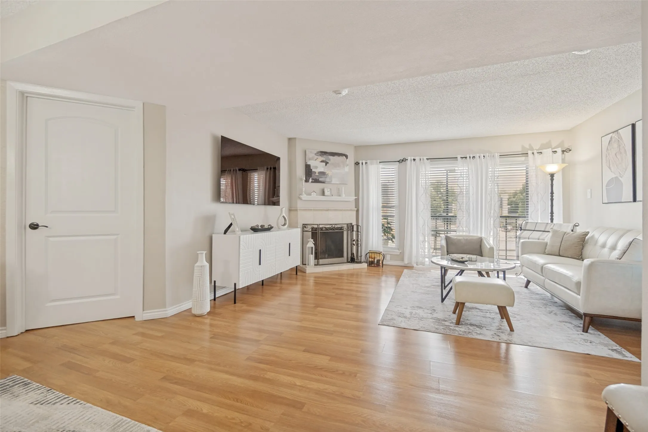 Open living area featuring wood-finish flooring, a built-in corner fireplace, and multiple windows with blinds and sheer curtains