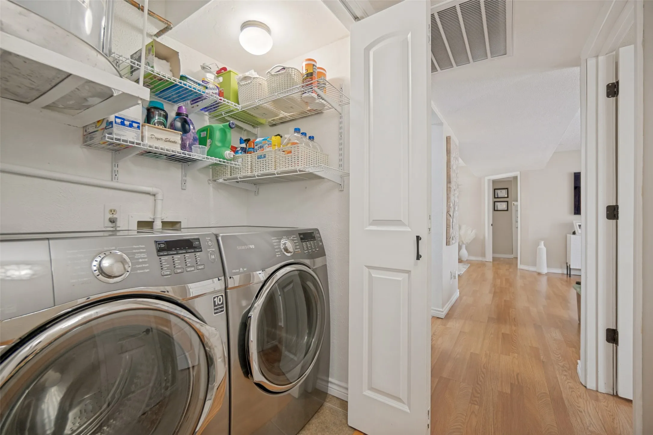 Dedicated laundry area featuring front-loading appliances, overhead wire shelving, and overhead lighting