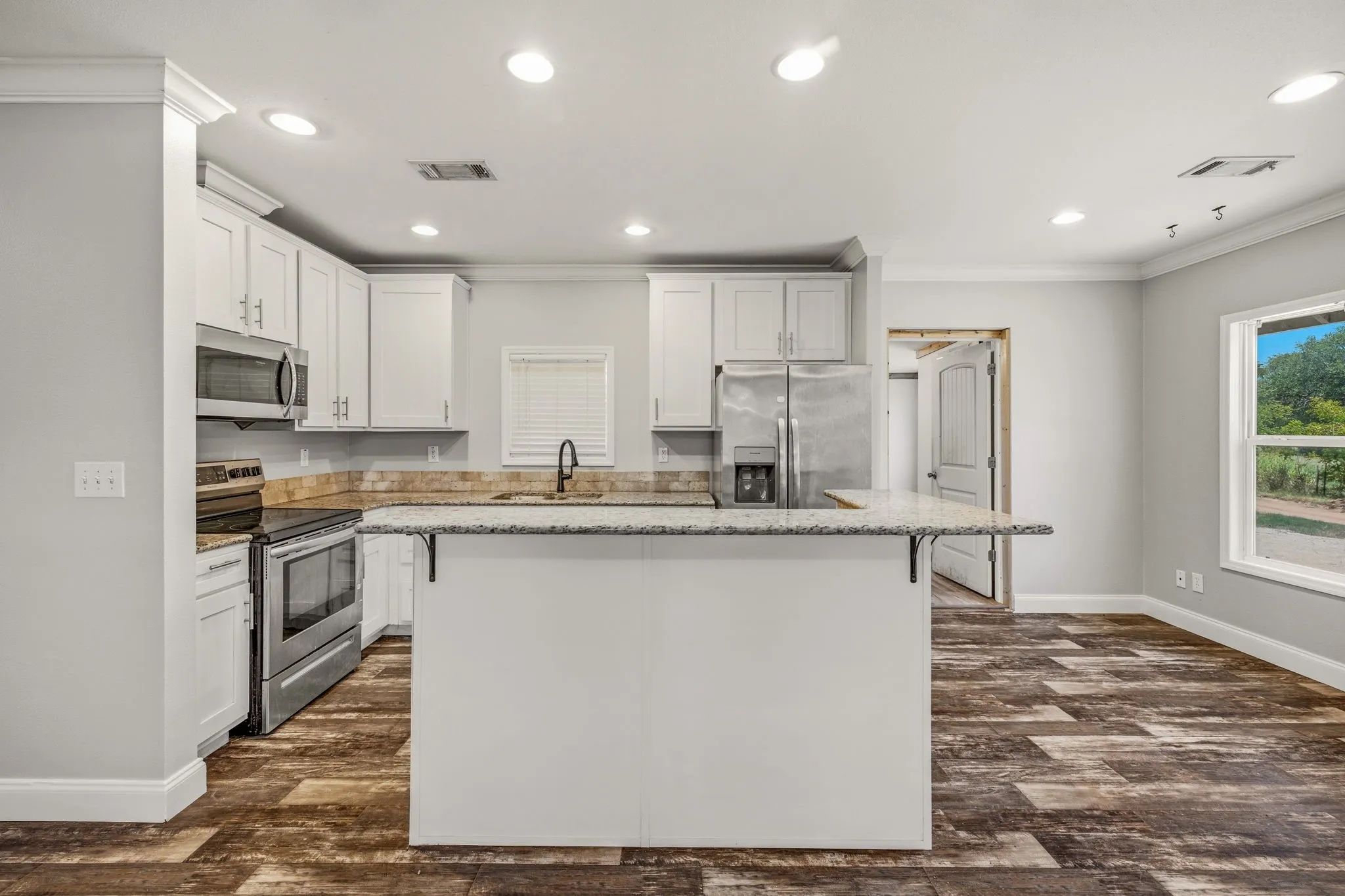 Kitchen with a peninsula island featuring granite countertops, white cabinetry, stainless steel appliances, wood-finish flooring, and recessed lighting
