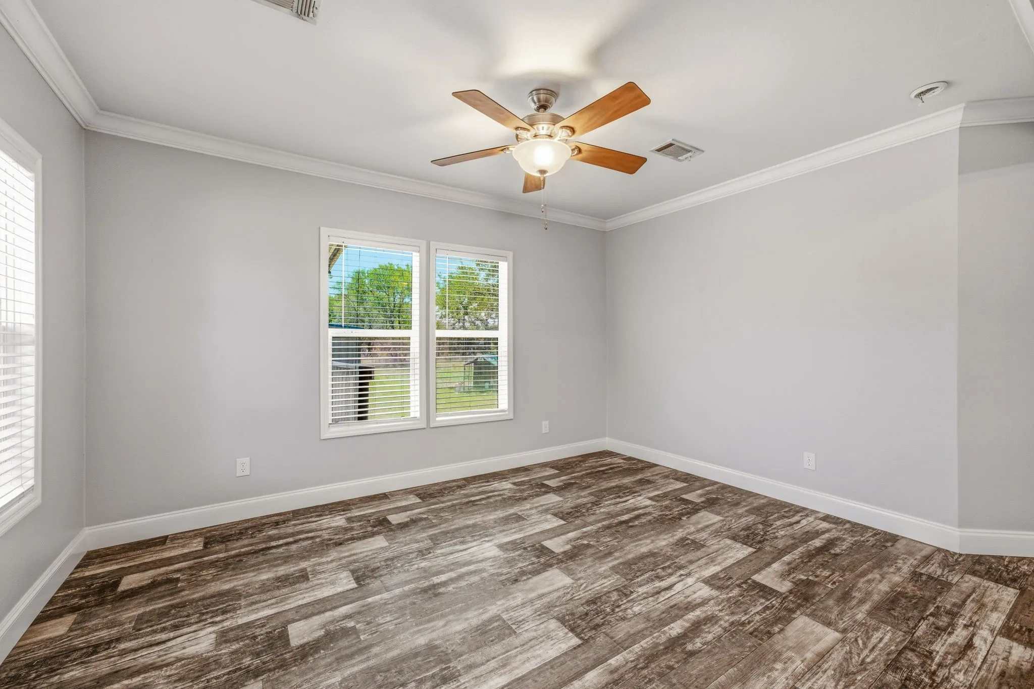 Spacious interior room featuring wood-finish flooring, light gray wall paint, and white crown molding