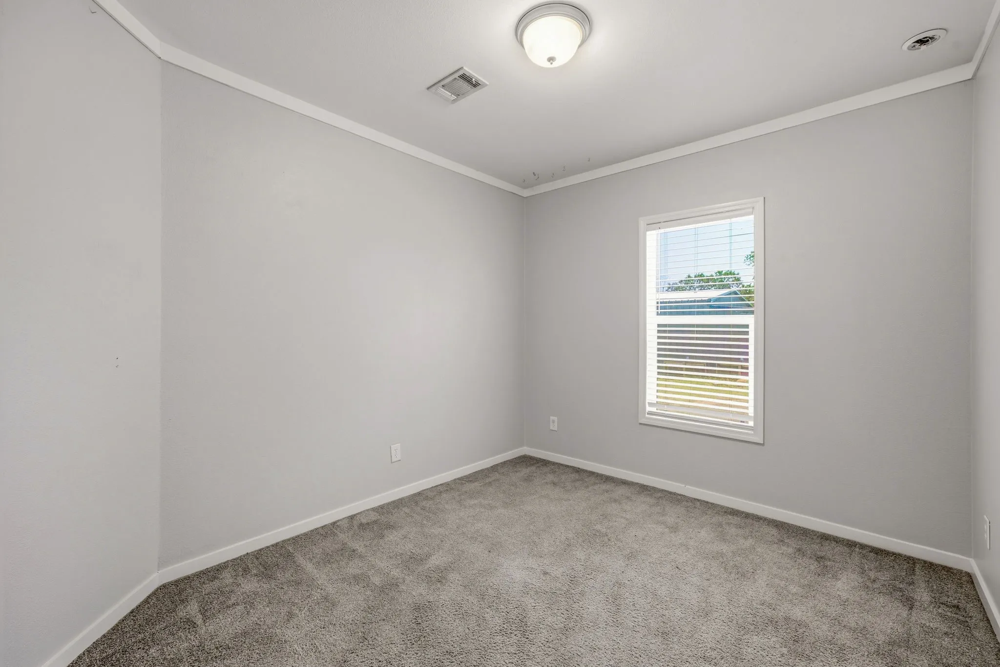 Bright interior space featuring a window with blinds, light gray wall paint, and gray carpet flooring