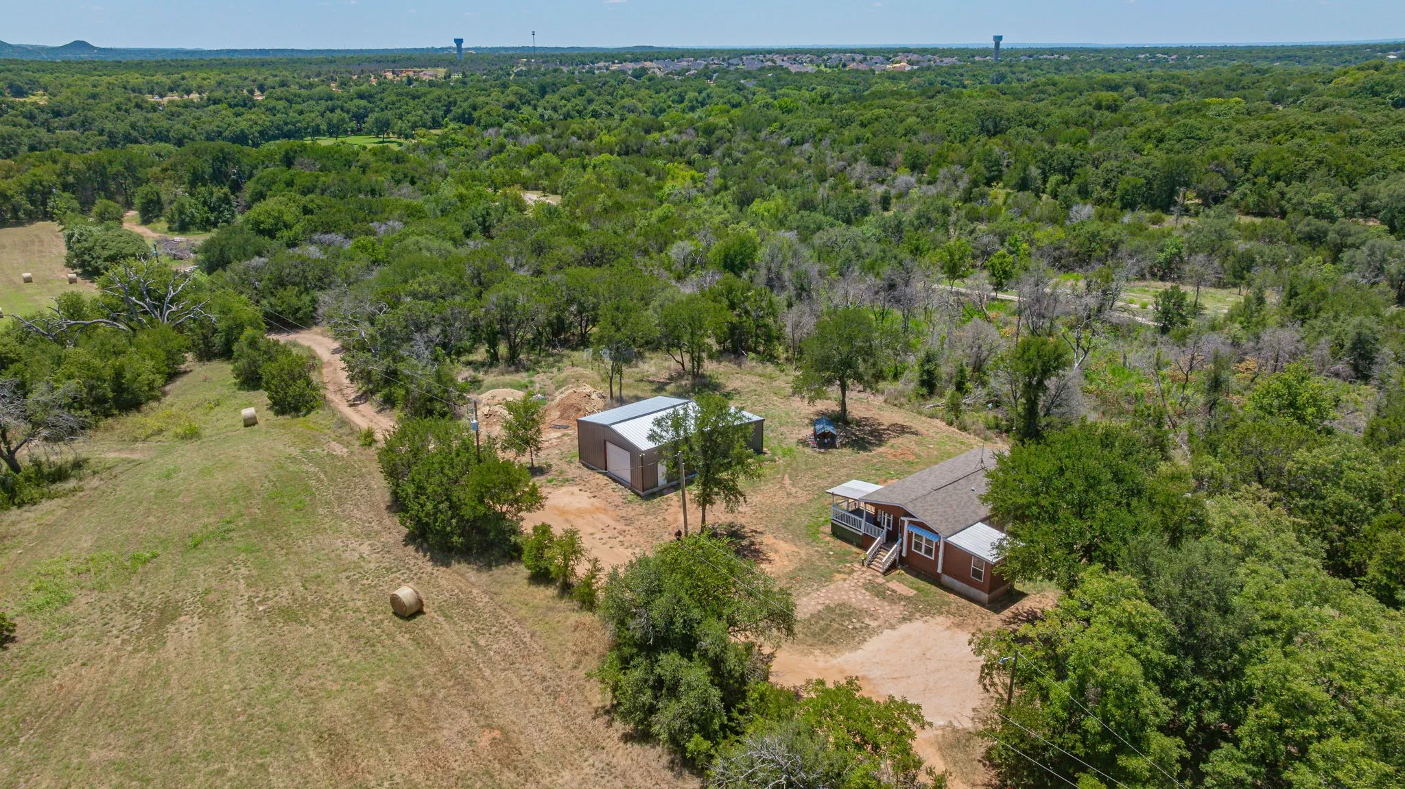 Expansive rural property featuring a brown ranch-style home with a covered porch, a separate metal-sided outbuilding, and significant tree coverage