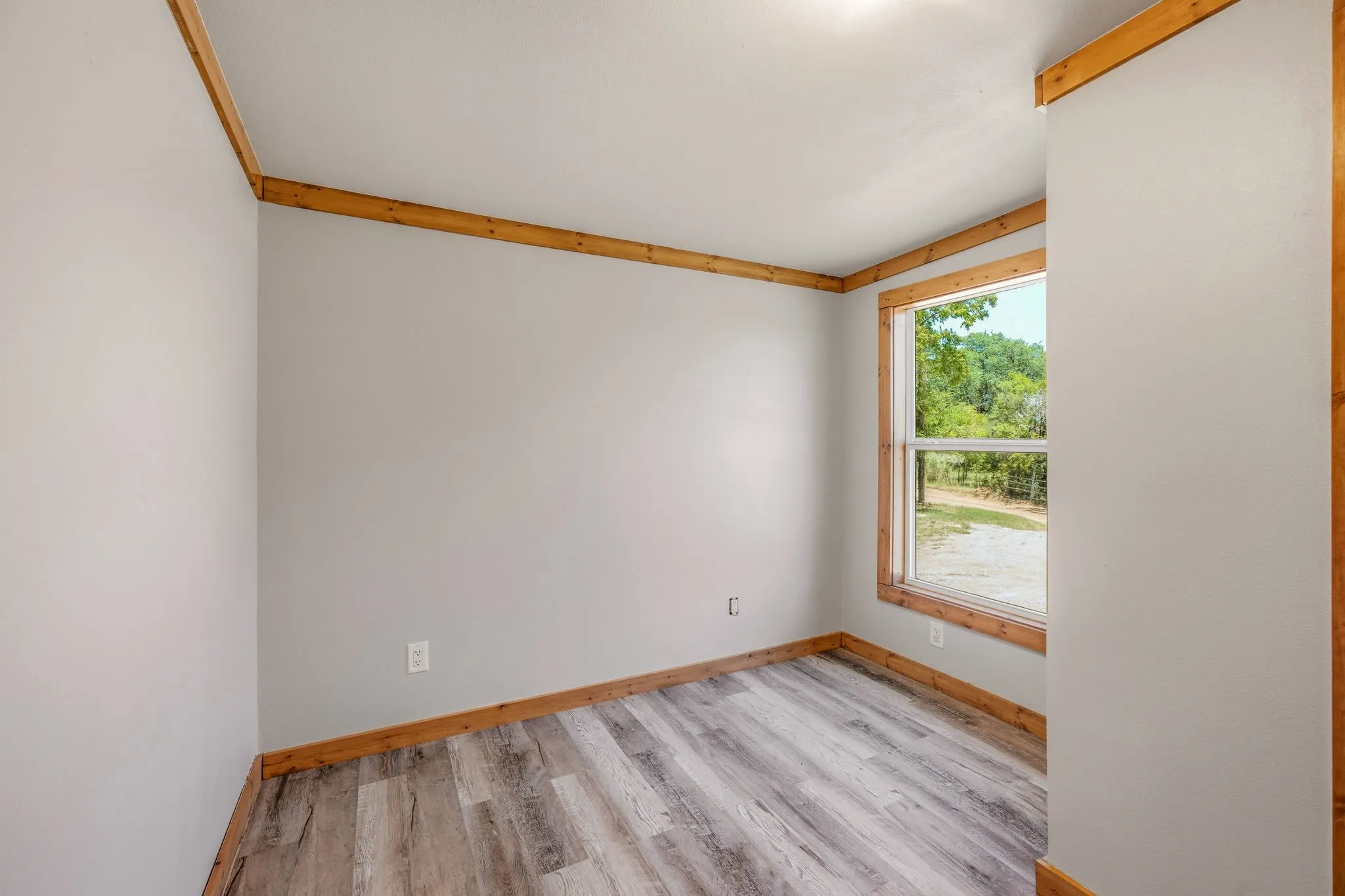 Interior room featuring light gray walls, wood-finish flooring, and natural wood trim around the window and ceiling
