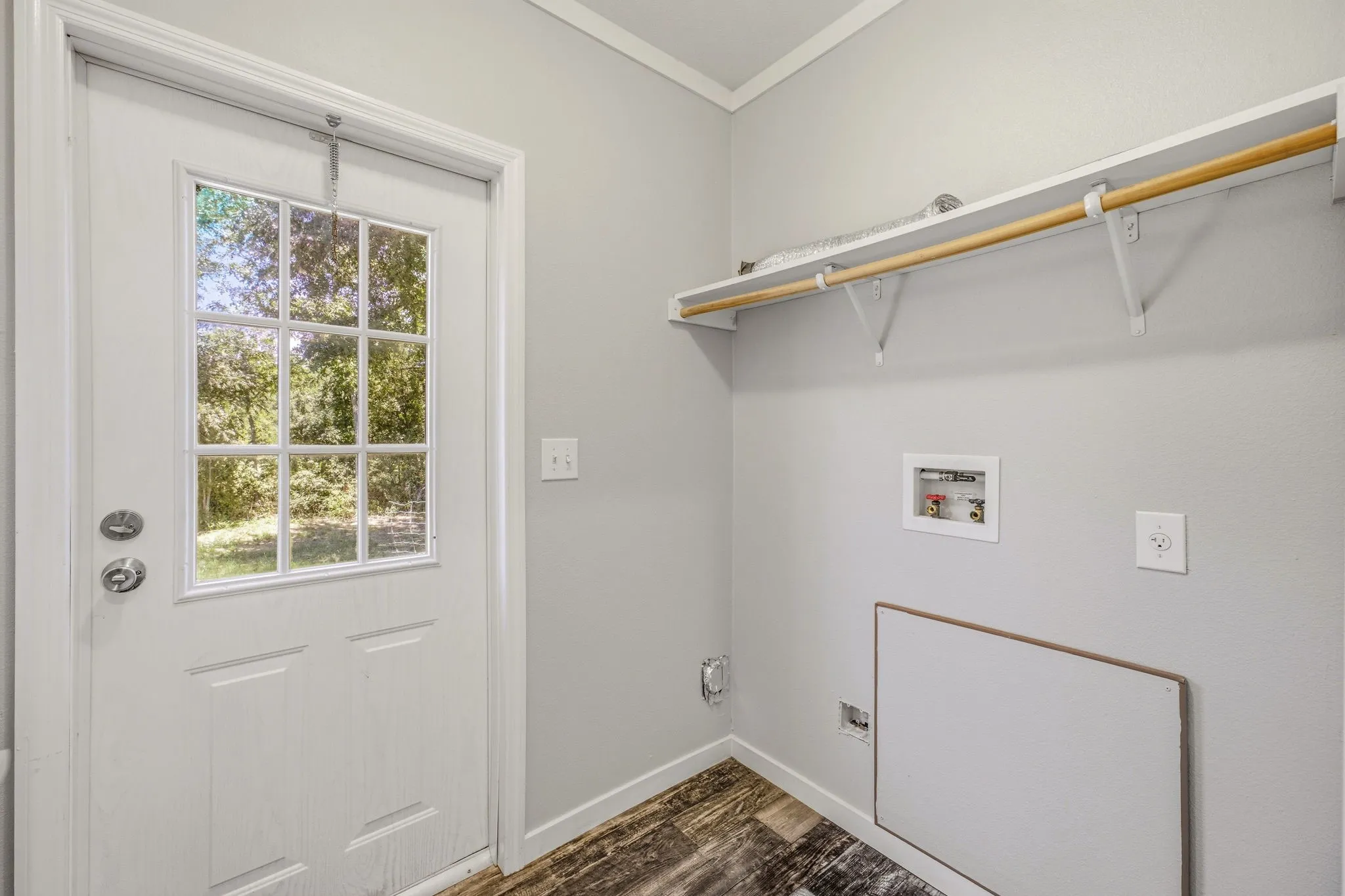 Utility area featuring a paneled door with divided light windows, wood-finish flooring, and a wall-mounted shelving unit with hanging rod