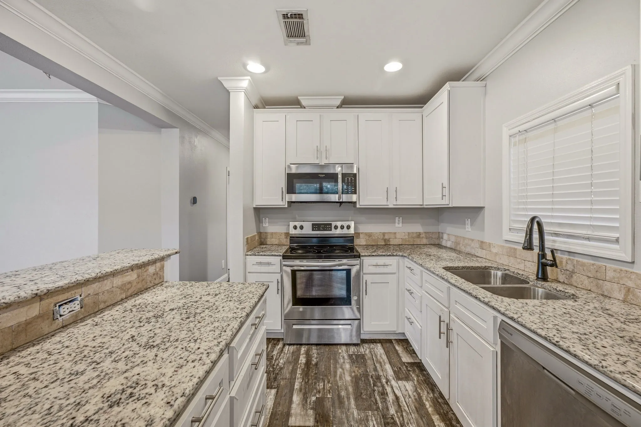 Kitchen featuring wood-finish flooring, light granite countertops, white shaker cabinetry, stainless steel appliances, and a mosaic tile backsplash