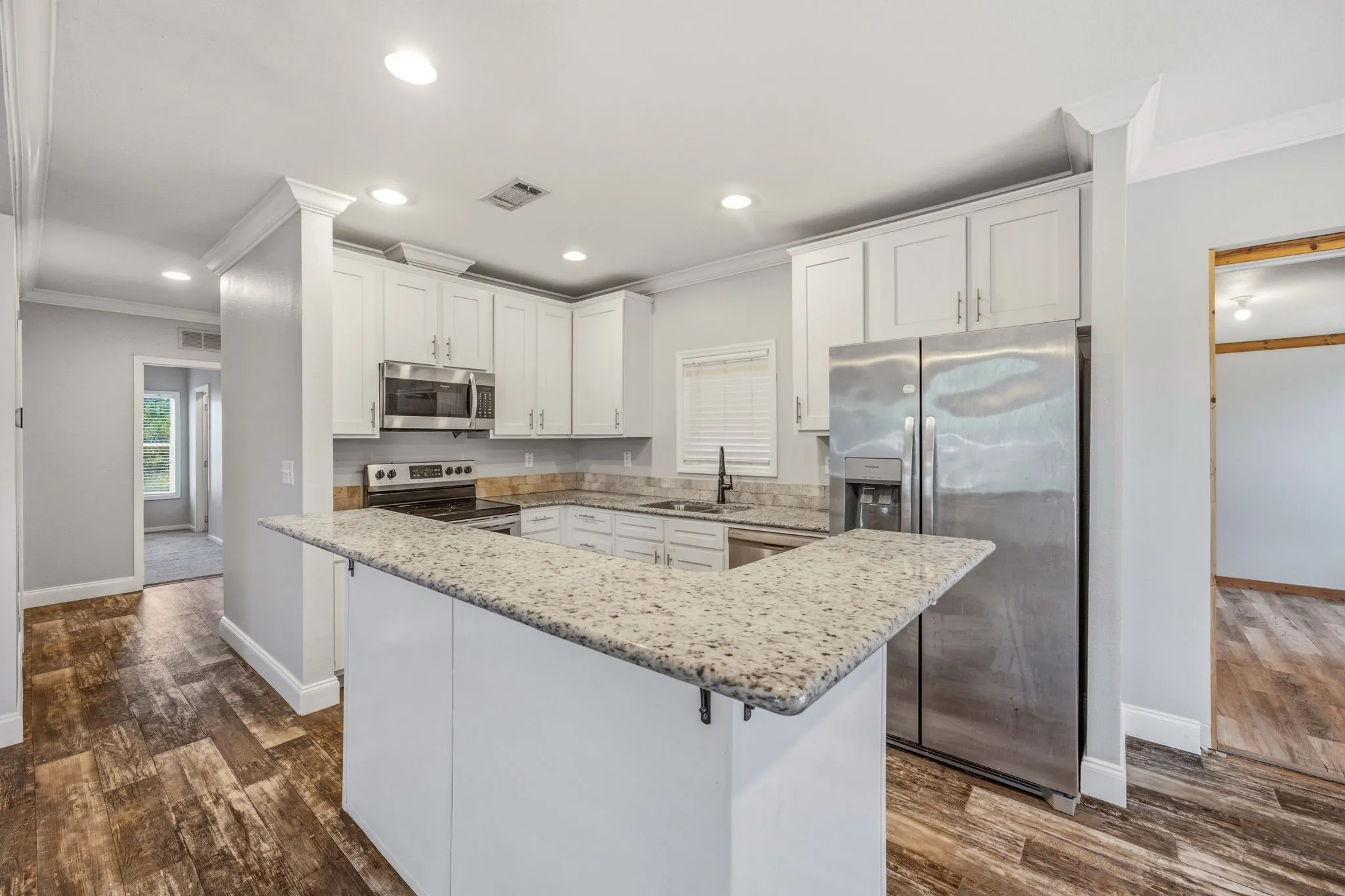 Modern kitchen featuring white cabinetry, light-colored speckled countertops, and stainless steel appliances