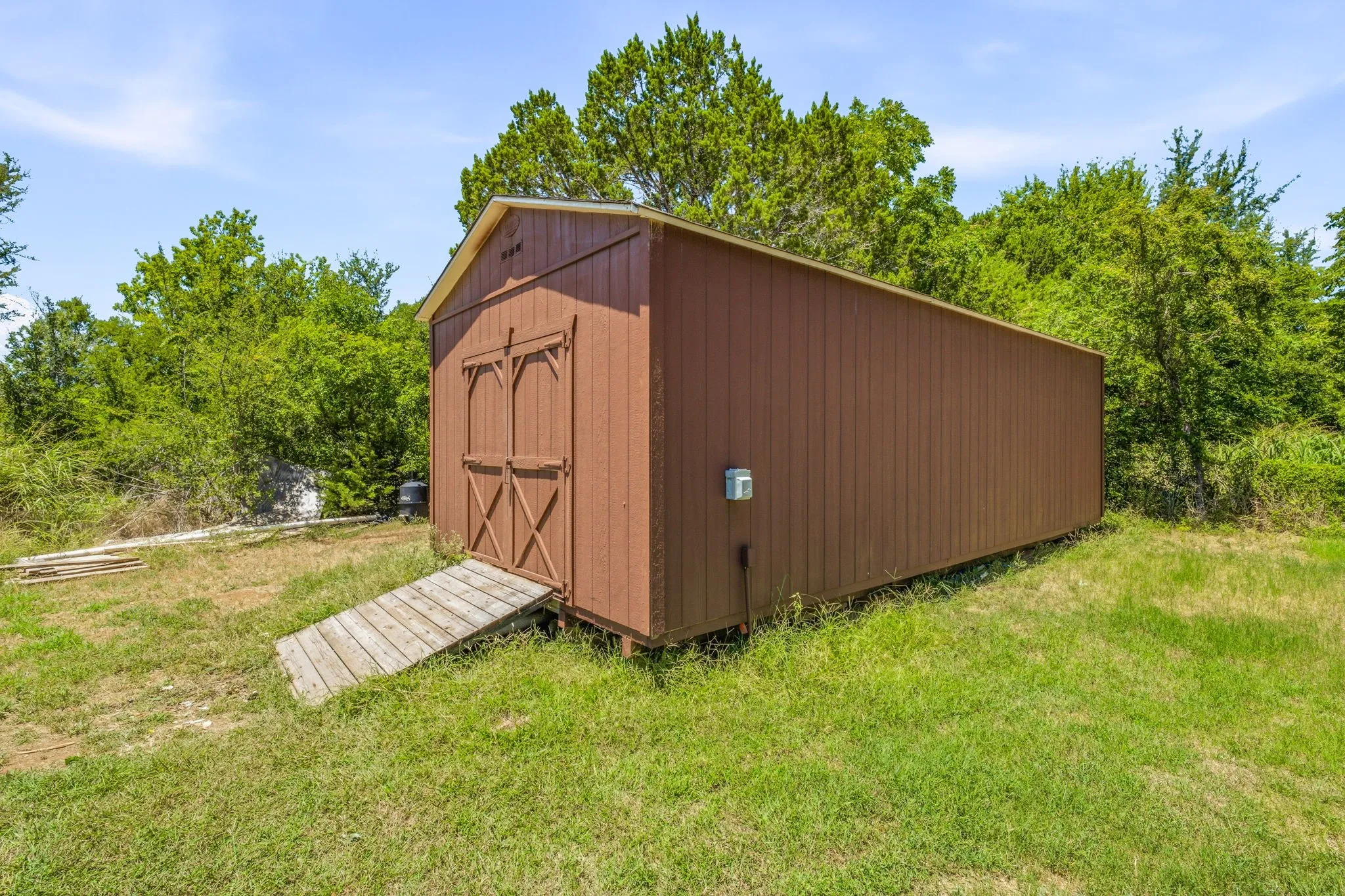Freestanding storage shed featuring brown board-and-batten siding, a gable roof, double barn doors, and a wood ramp entry