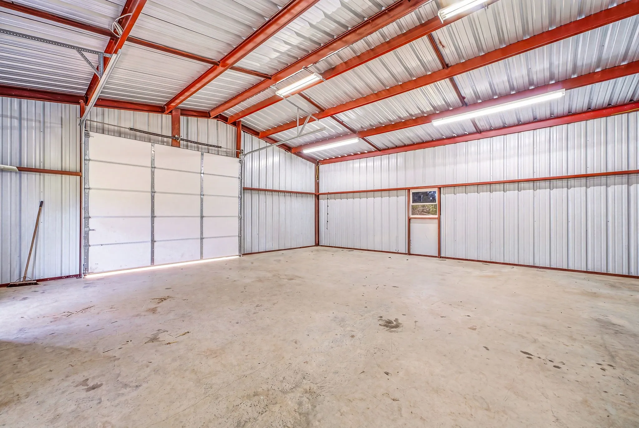 Spacious metal structure featuring a concrete floor, large overhead door, interior personnel door, and functional windows
