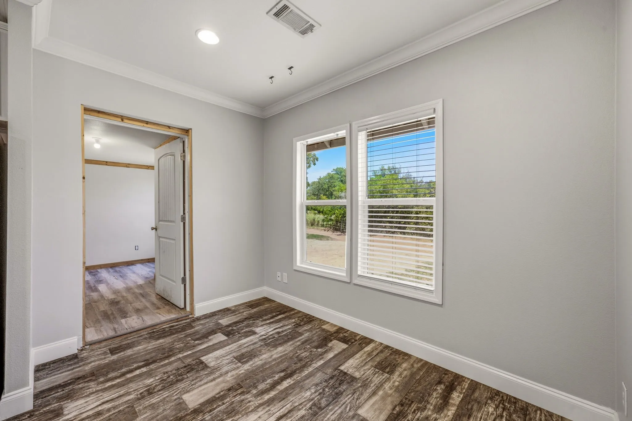 Room featuring wood-finish flooring, two windows with blinds, light gray walls, white baseboards, and crown molding