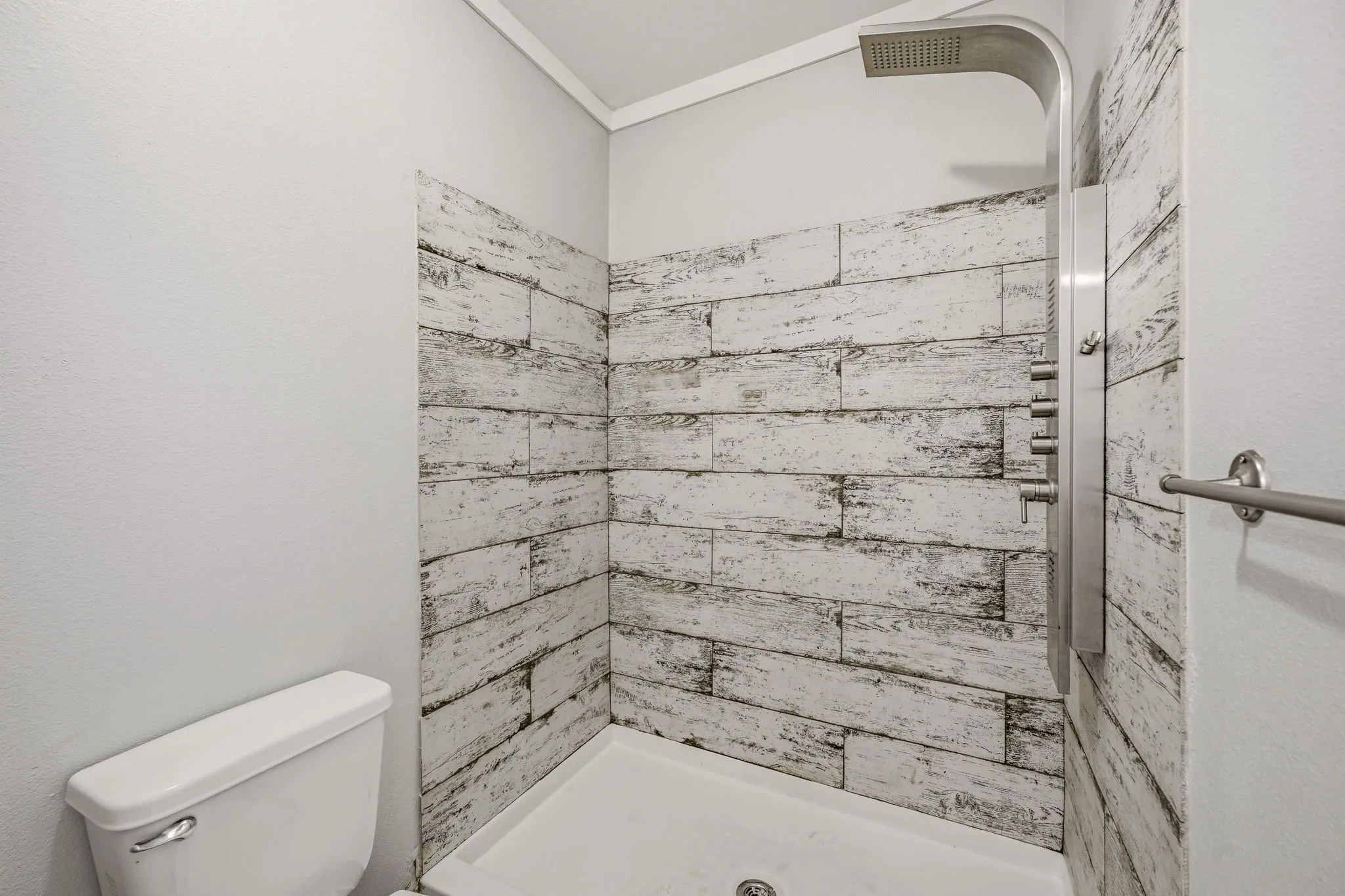 Shower stall featuring distressed wood-look wall tile and a multi-function shower panel with an overhead rain shower