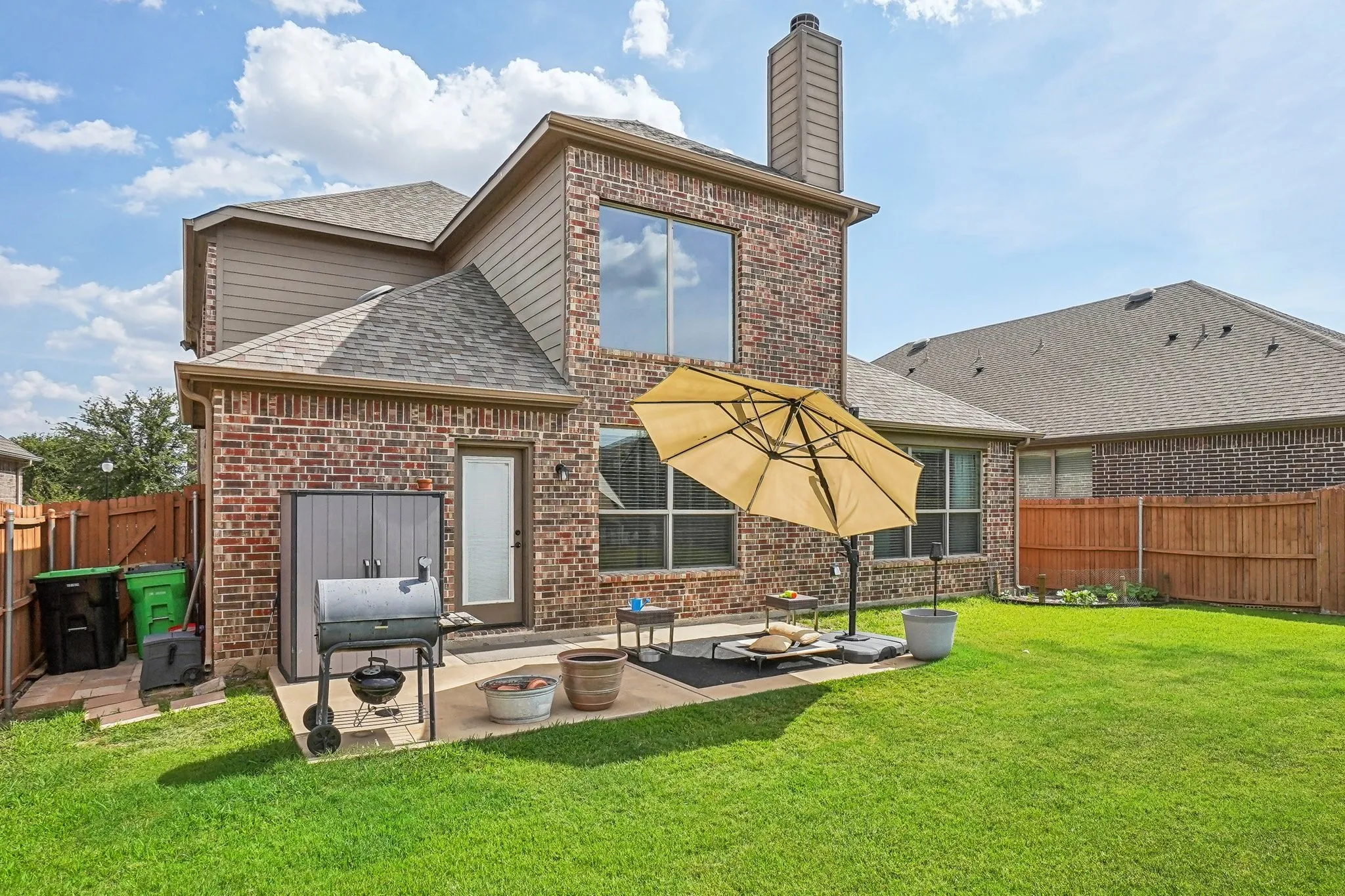 Rear view of property featuring brick siding, a fenced backyard, roof with shingles, and a patio