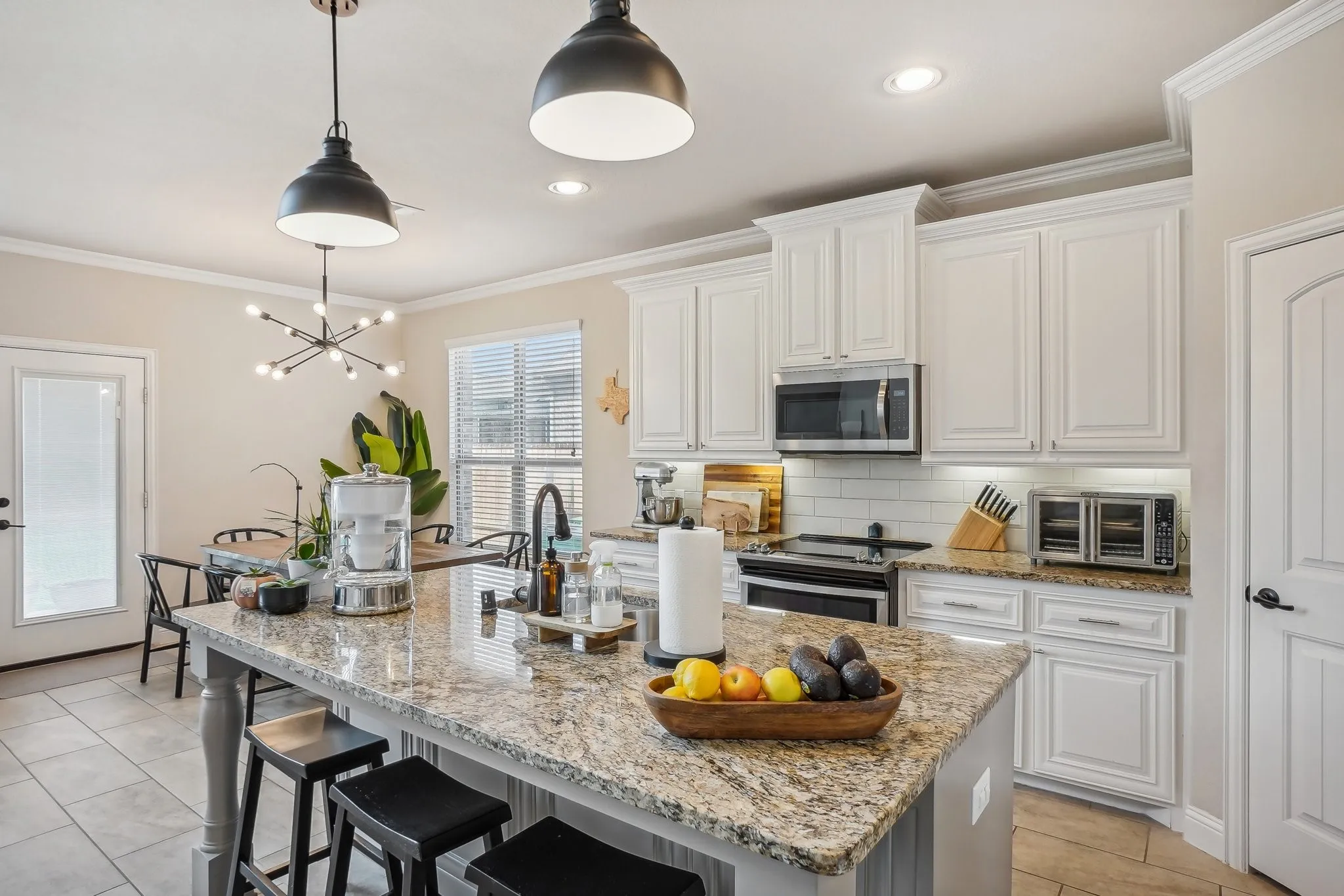 Kitchen with crown molding, a breakfast bar, light stone countertops, decorative light fixtures, and white cabinetry