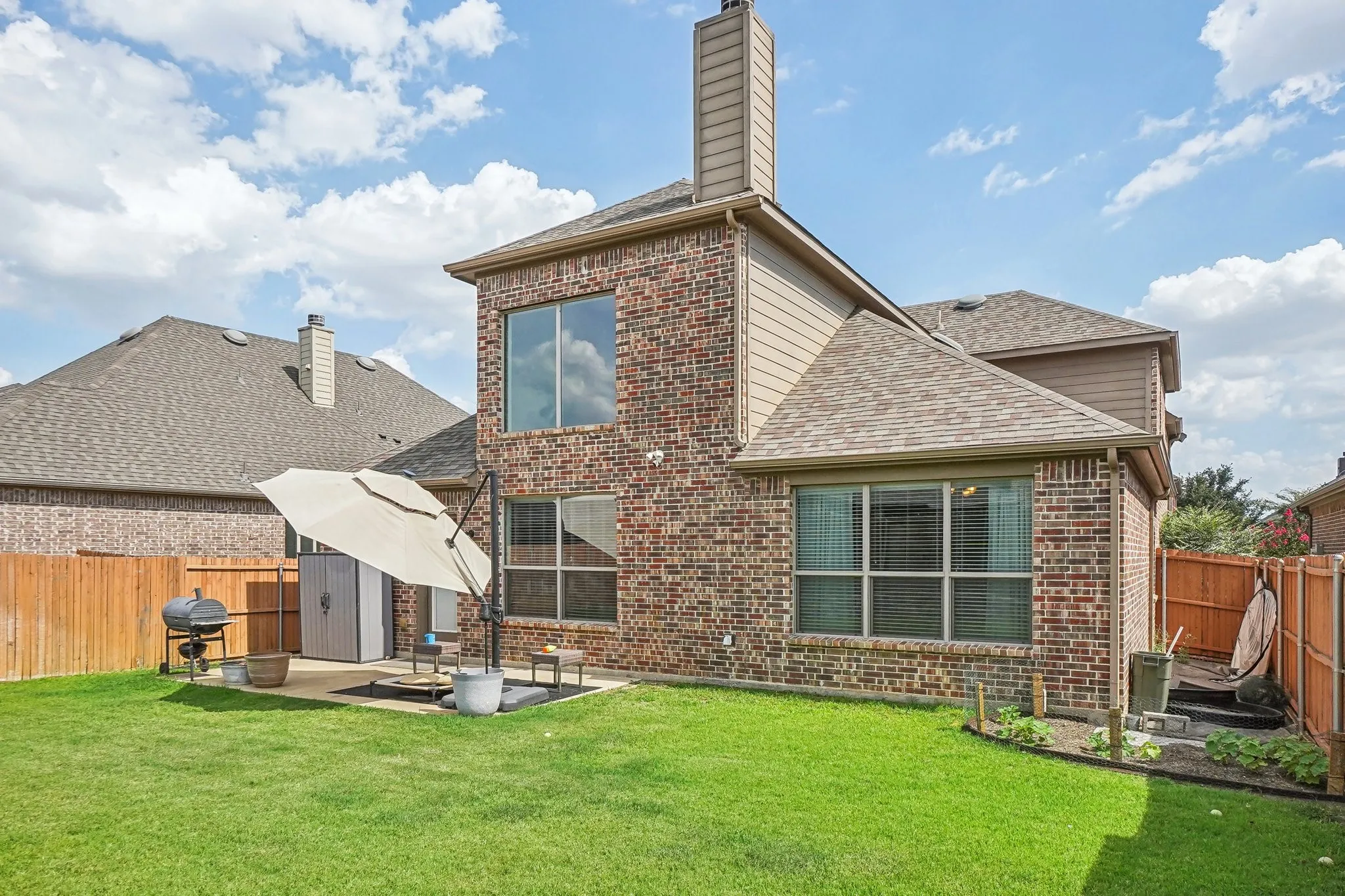 Back of property featuring a fenced backyard, roof with shingles, brick siding, a chimney, and a patio