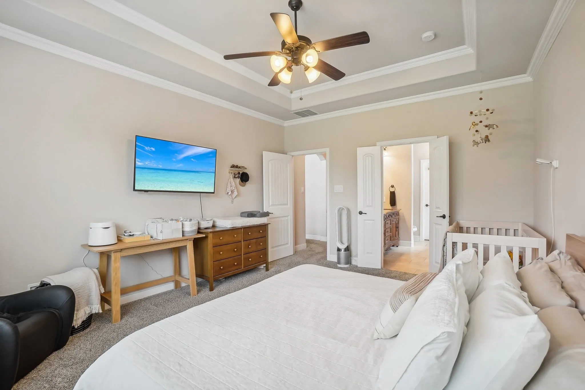 Bedroom with a raised ceiling, ornamental molding, a ceiling fan, carpet, and ensuite bath