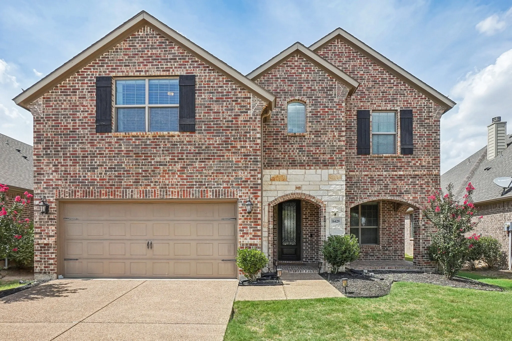 View of front of property featuring brick siding, a garage, concrete driveway, a front lawn, and stone siding
