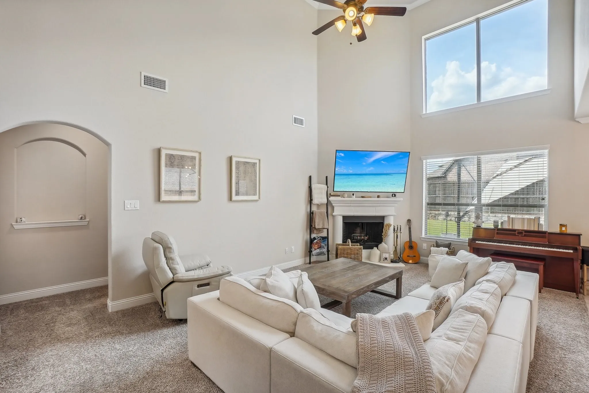 Carpeted living room with a fireplace, ceiling fan, and a high ceiling