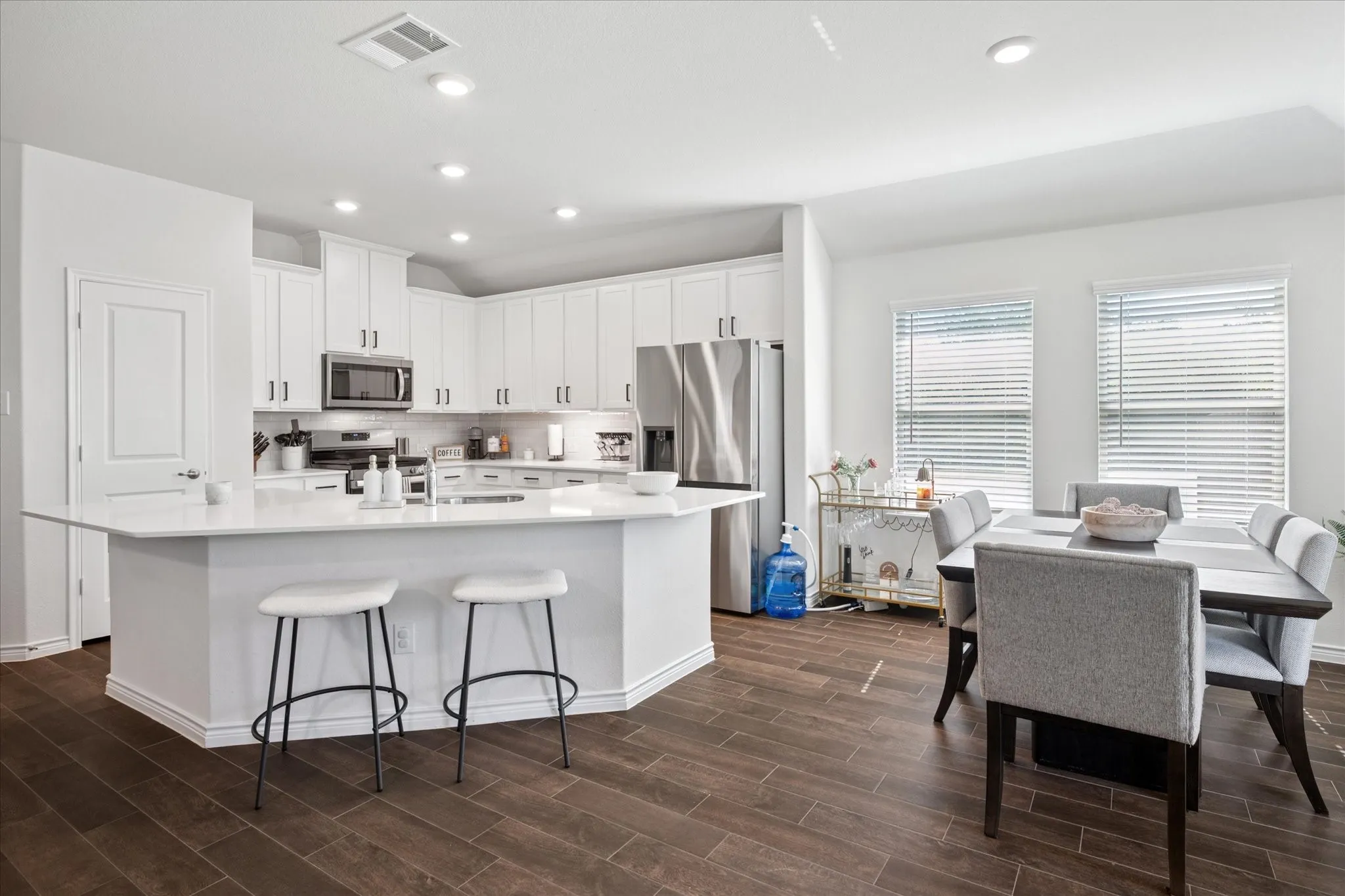 White kitchen with stainless steel appliances, recessed lighting, and wood-finish flooring