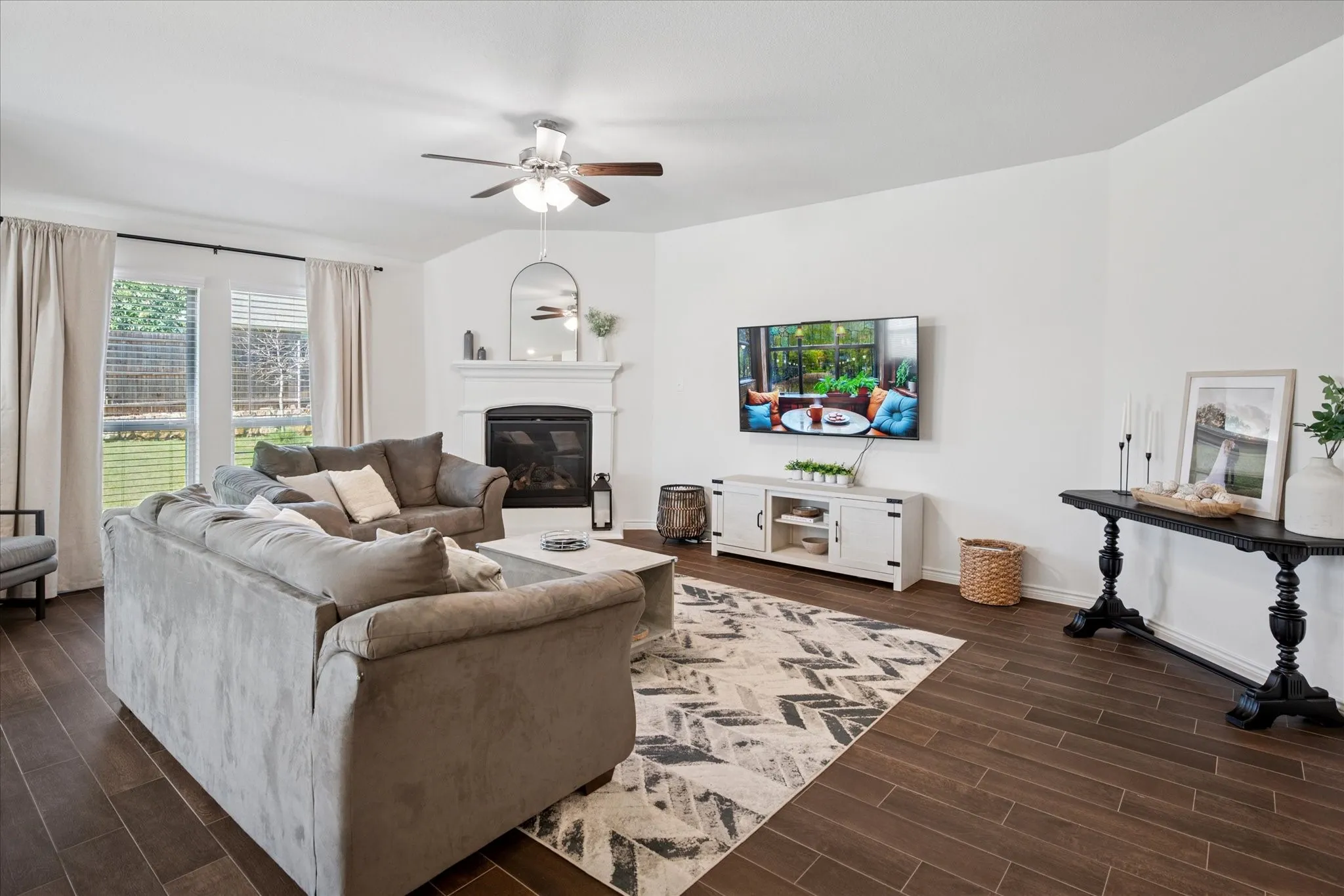 Spacious living area featuring wood-finish flooring, a ceiling fan, and large windows with horizontal blinds