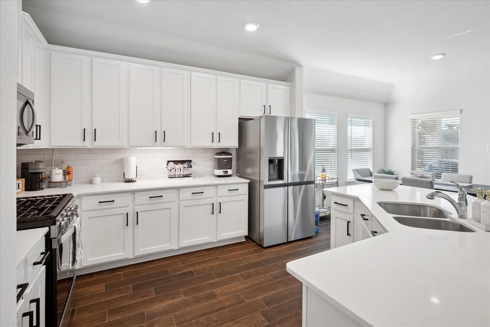 Bright kitchen featuring white shaker cabinetry with matte black hardware, white subway tile backsplash, stainless steel appliances, and wood-finish flooring