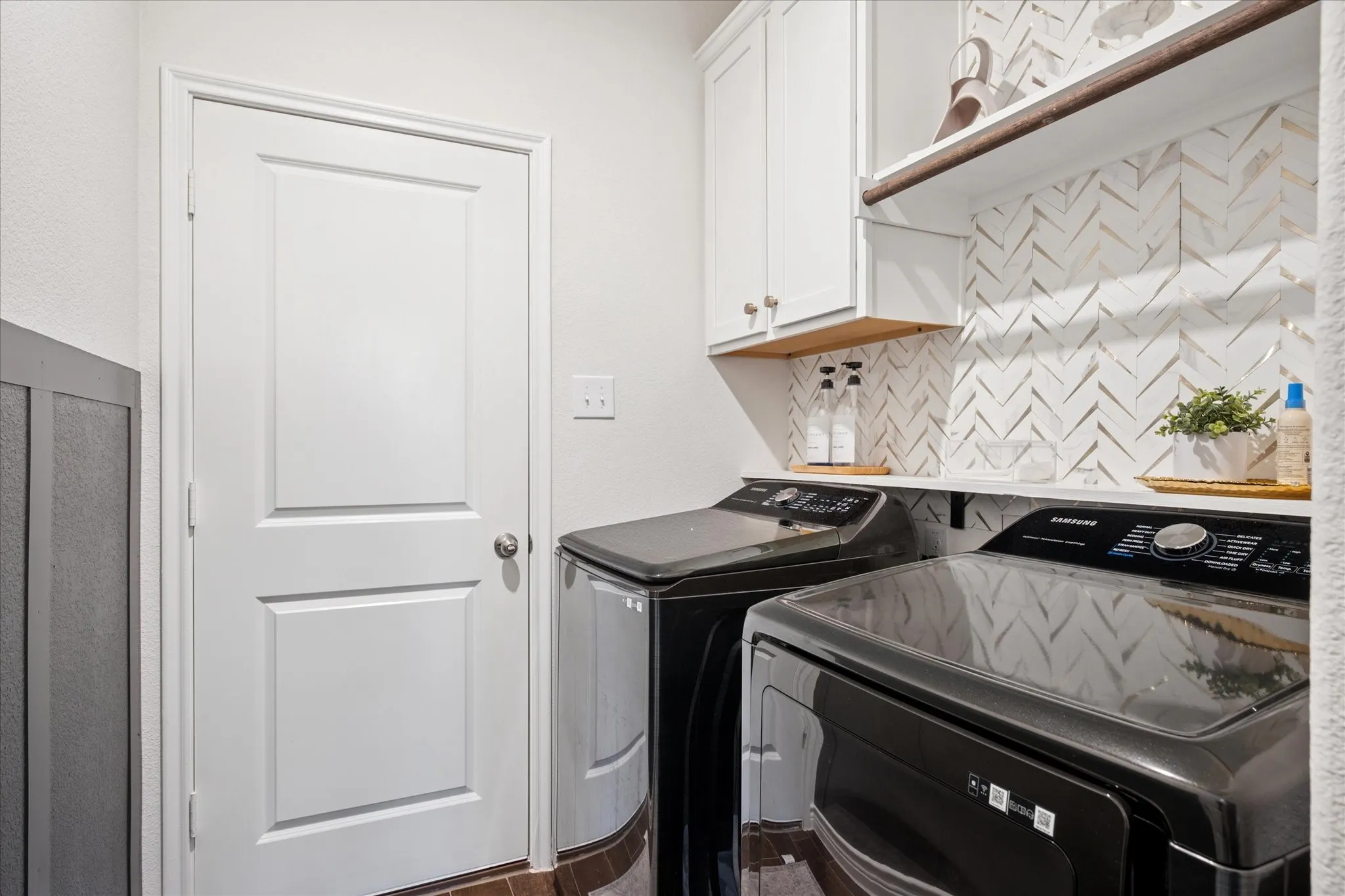 Laundry area featuring a herringbone tile backsplash, white shaker-style cabinetry, a wood-finish open shelf, and a dark board and batten accent wall