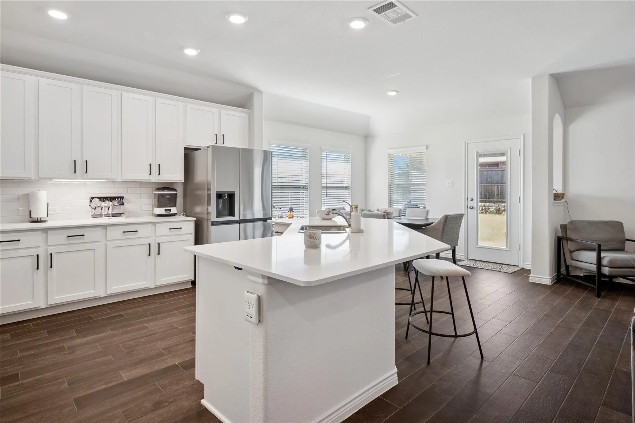 Open-concept kitchen featuring an oversized island with countertop seating, white shaker cabinetry, stainless steel appliances, white subway tile backsplash, and dark wood-finish flooring