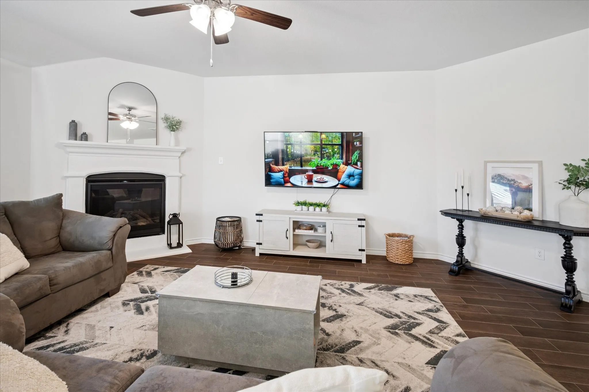 Living area featuring a fireplace with a white mantel, dark wood-finish flooring, a ceiling fan, and vaulted ceilings
