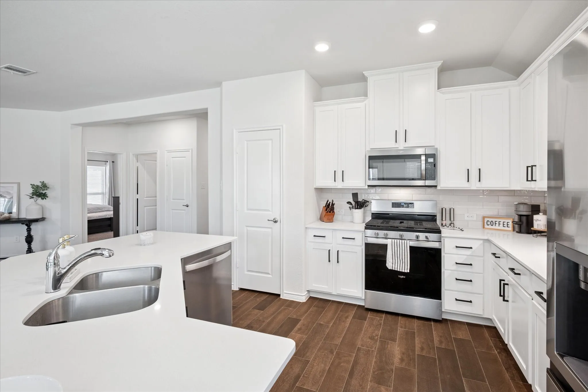 Bright kitchen featuring white cabinetry with black hardware, stainless steel appliances, solid surface countertops, and wood-finish flooring
