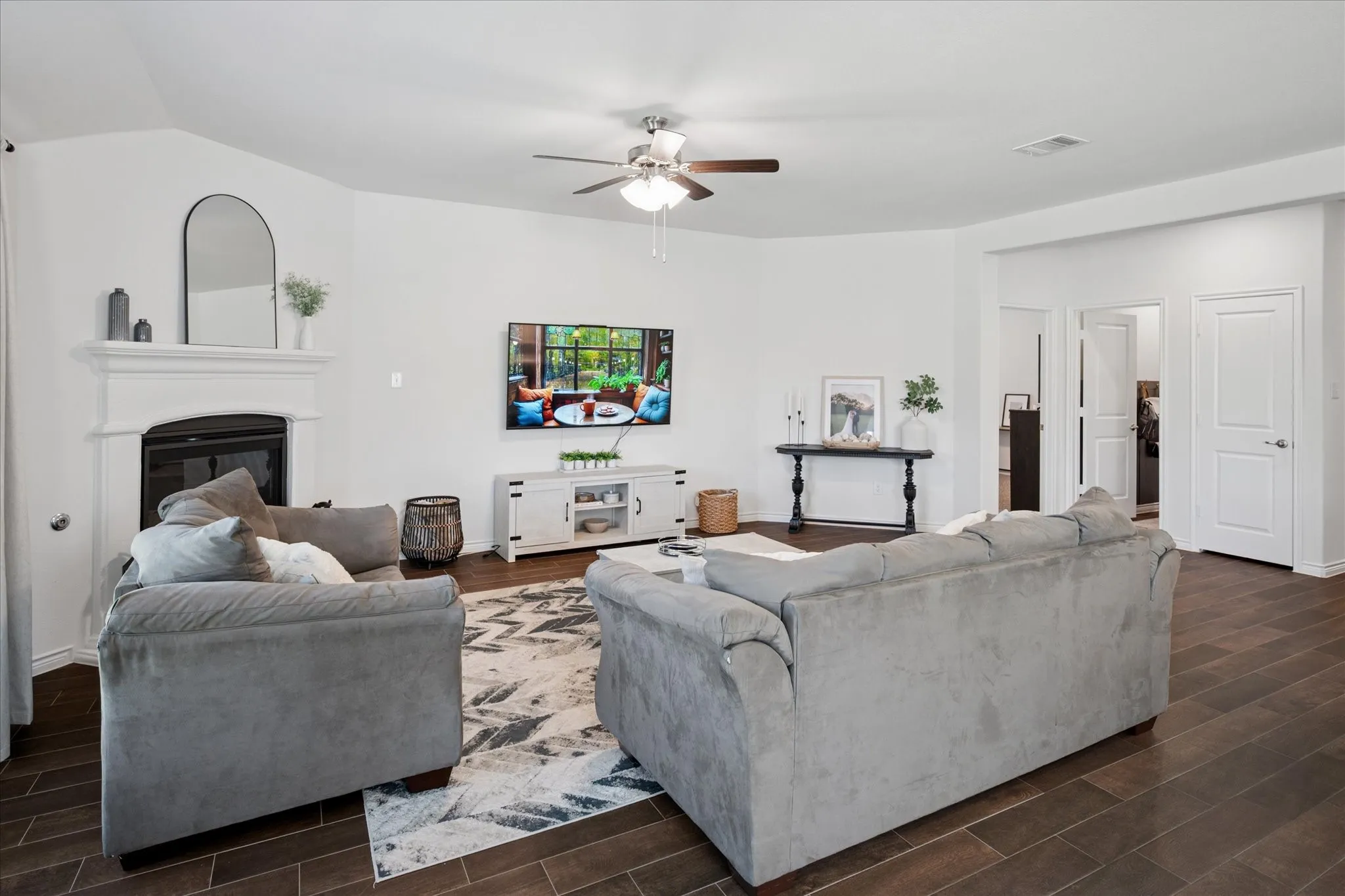 Spacious living area featuring a built-in fireplace with a white mantle, dark wood-finish flooring, and a ceiling fan with integrated lighting