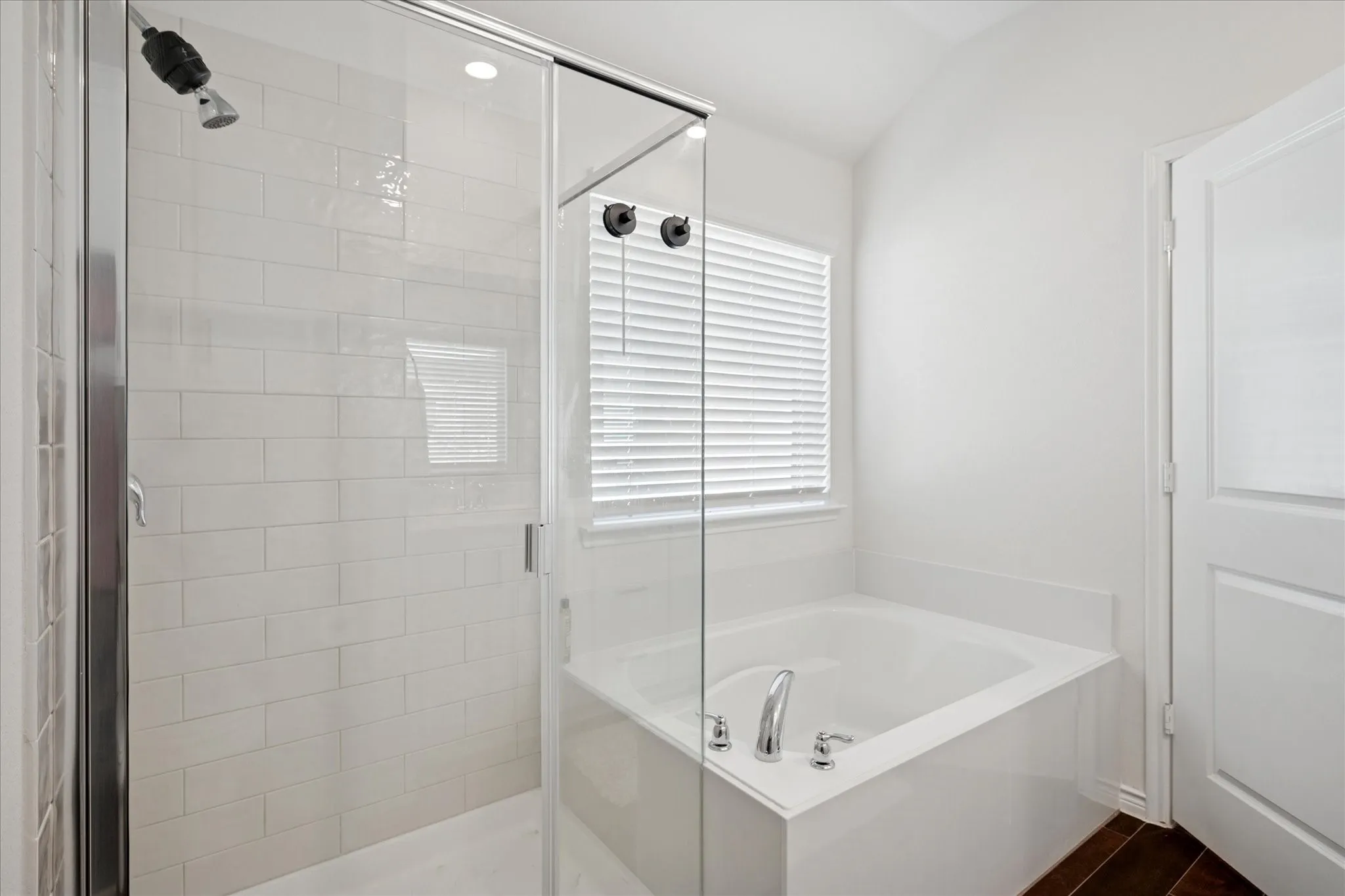 Bathroom featuring a built-in tub with deck-mounted chrome fixtures, a separate shower with subway tile surround and glass enclosure, a window with horizontal blinds, and wood-finish flooring