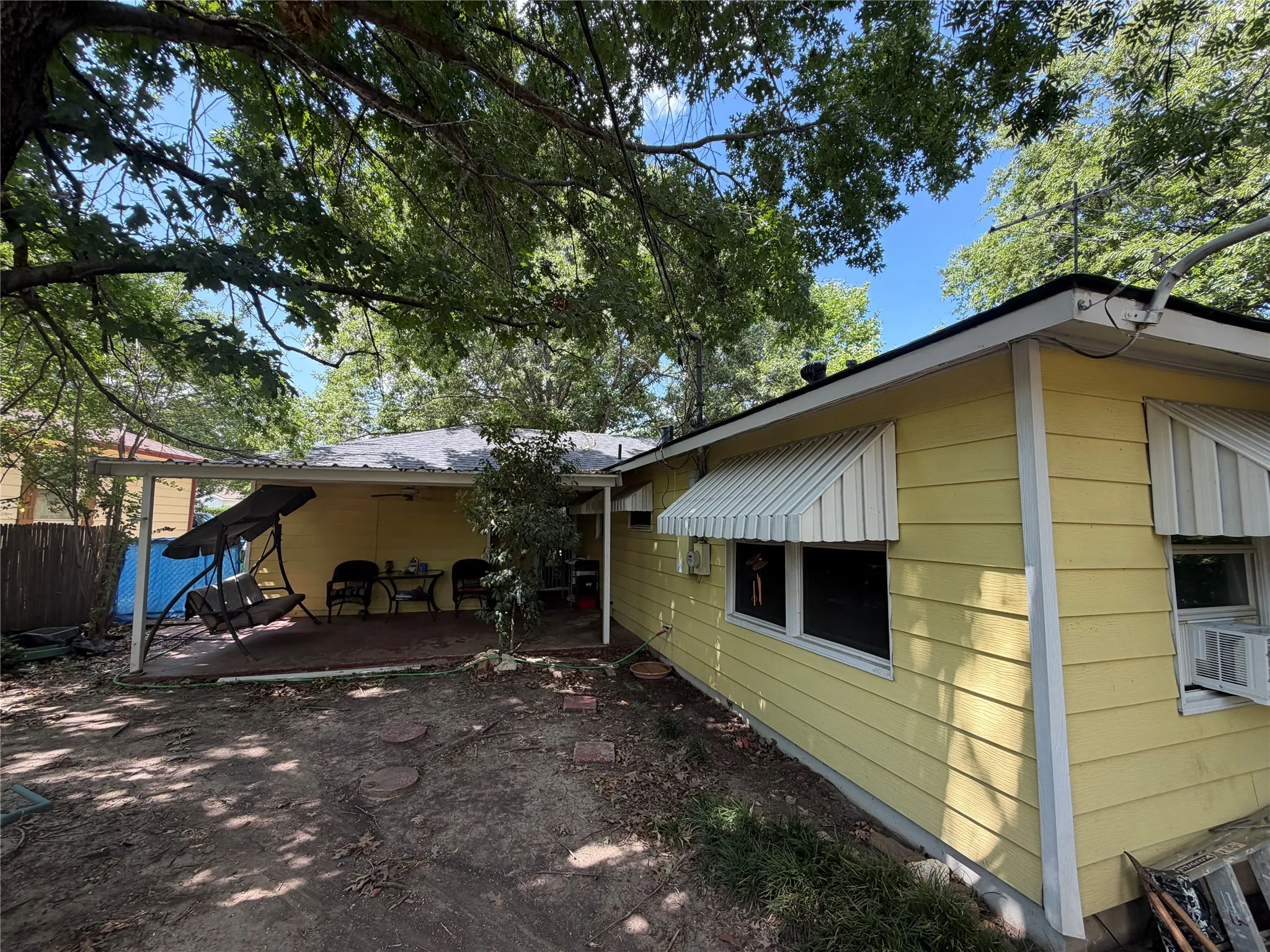 Exterior featuring yellow siding, a covered patio with a dark-colored surface, and striped window awnings