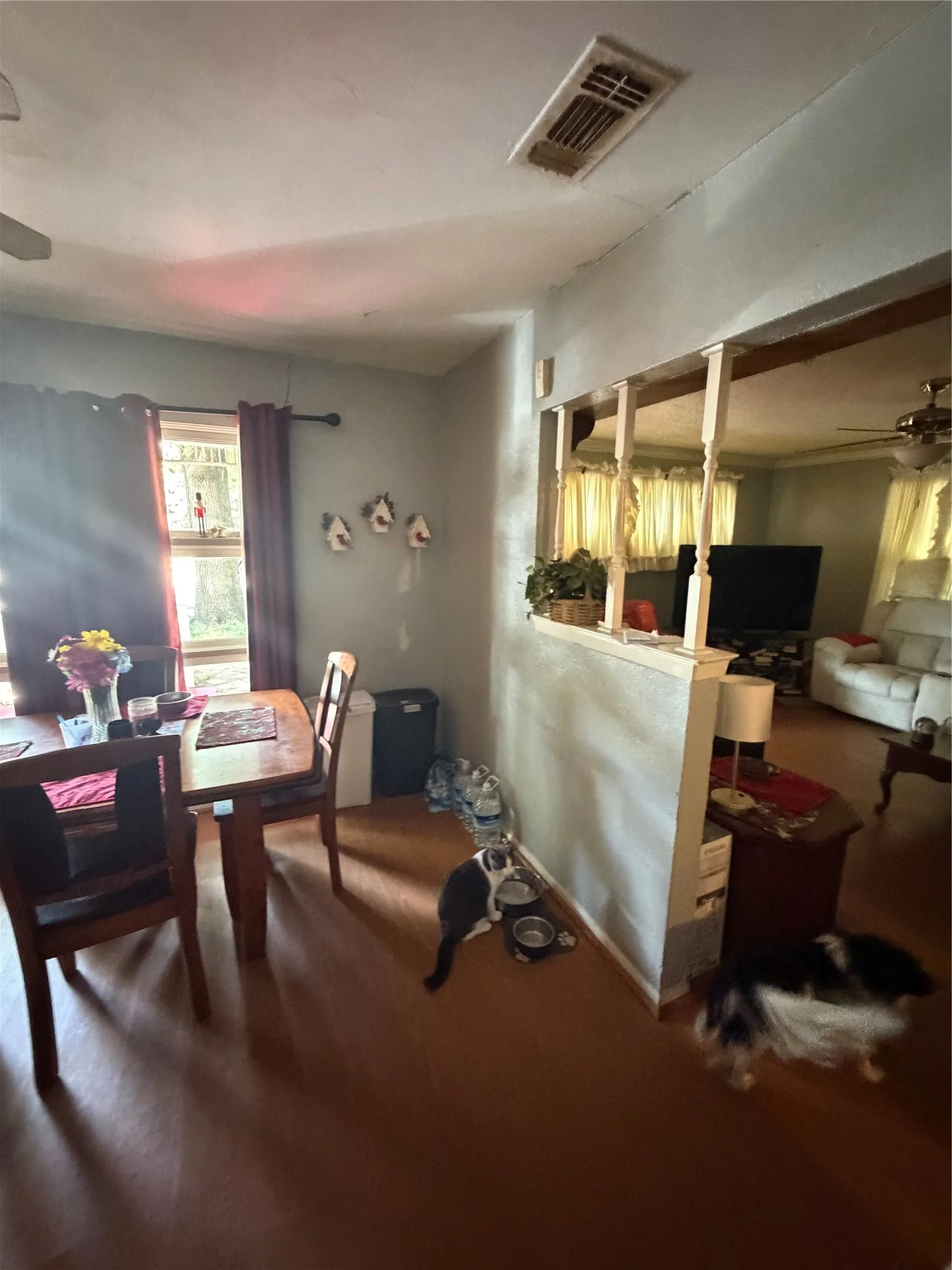 Dining area featuring wood-finish flooring, a window with dark curtains, and a ceiling-mounted ventilation register