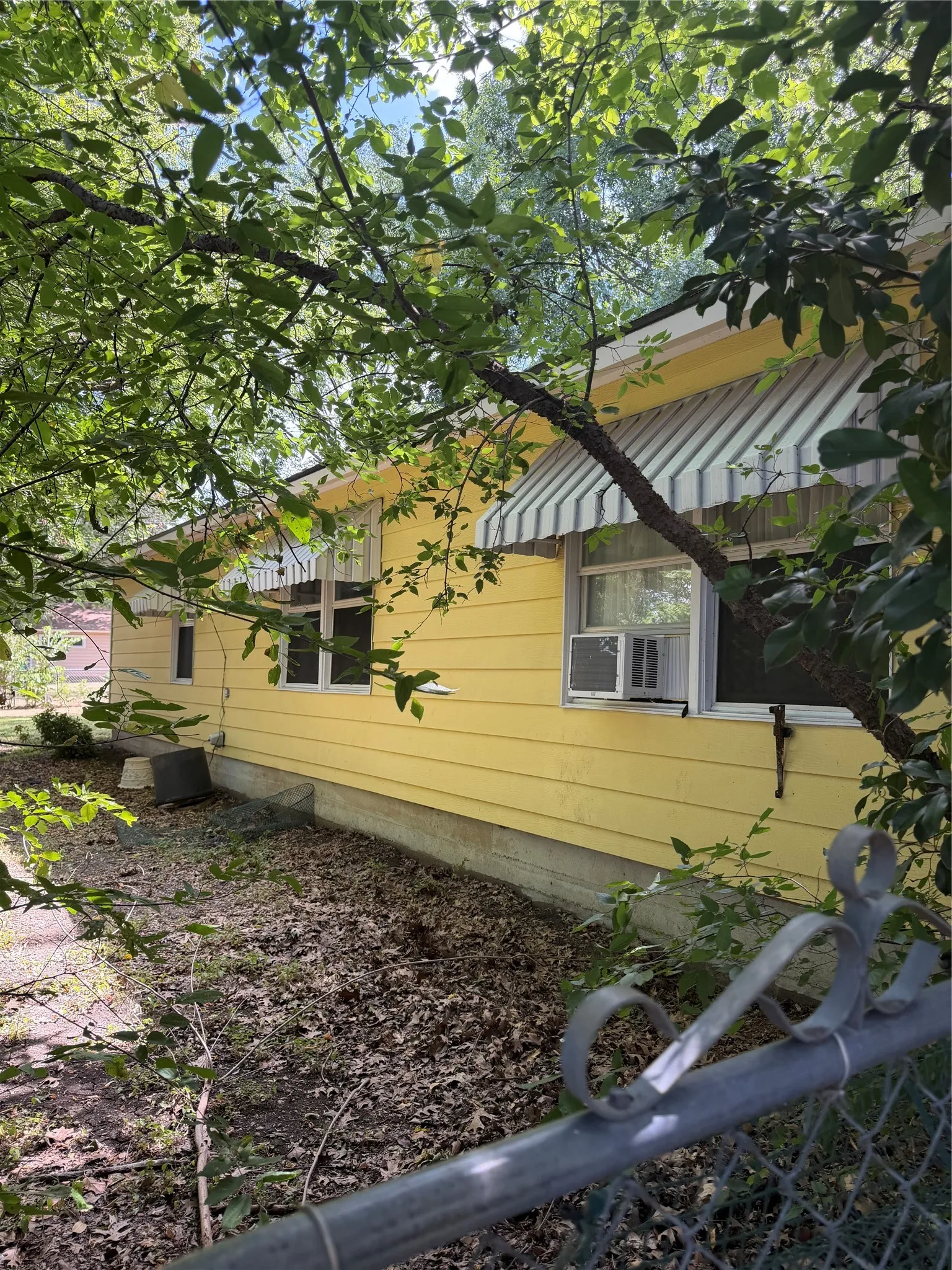 Yellow exterior siding with multiple windows, a window-mounted air conditioning unit, and a striped window awning